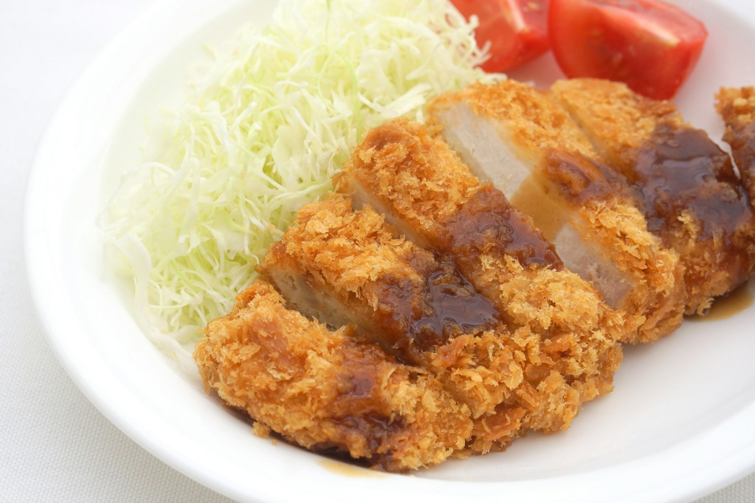 Panierte Schweinekotelett serviert mit gehobeltem Kohl und Tomatenscheiben