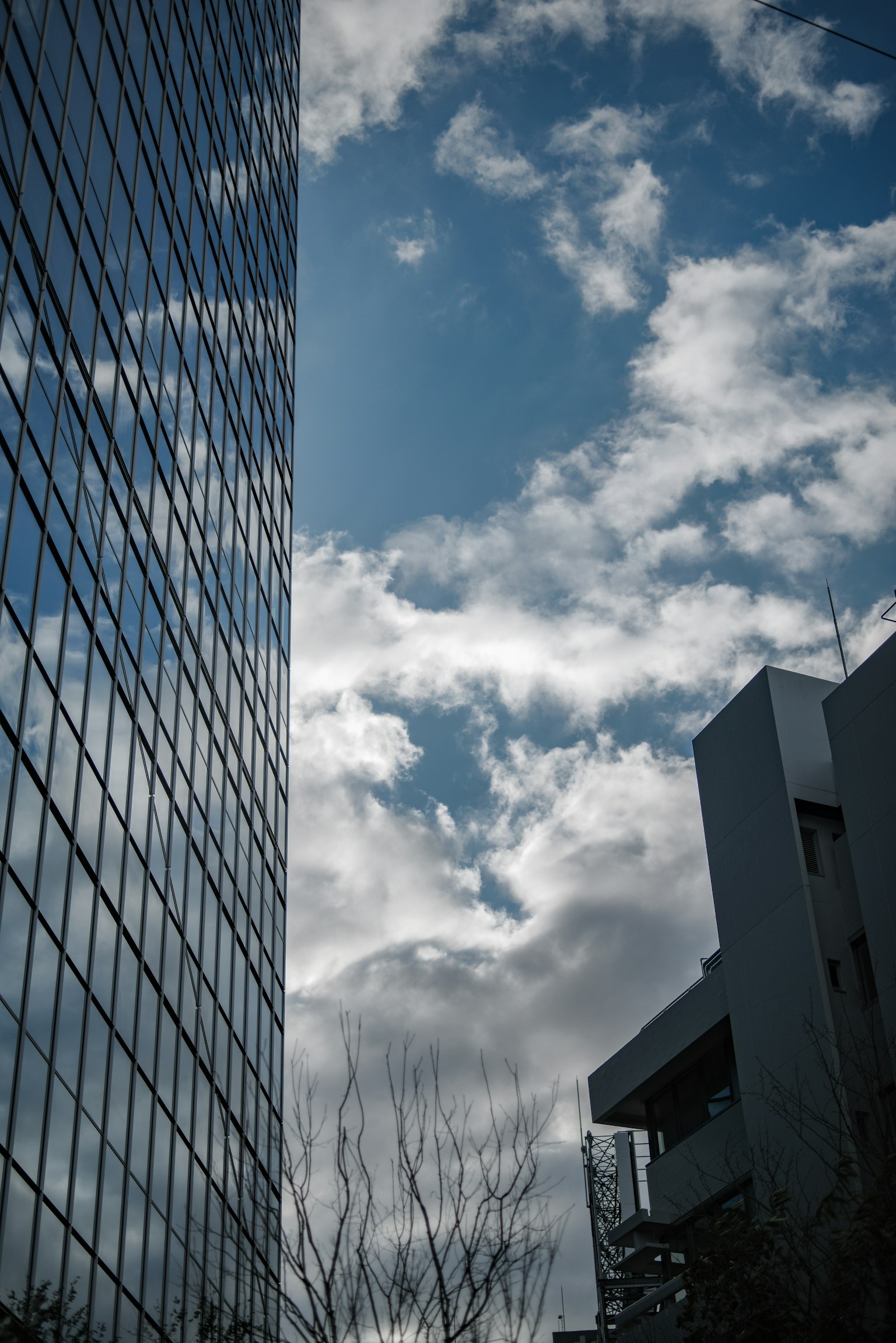 Mur en verre d'un gratte-ciel reflétant le ciel bleu et les nuages avec un bâtiment voisin