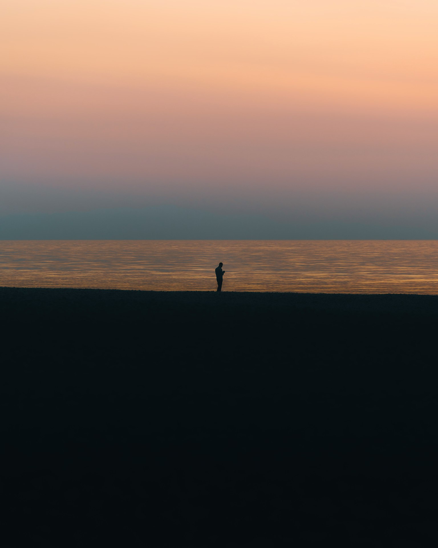 Silhouette di una persona in piedi su una spiaggia al tramonto con acqua calma