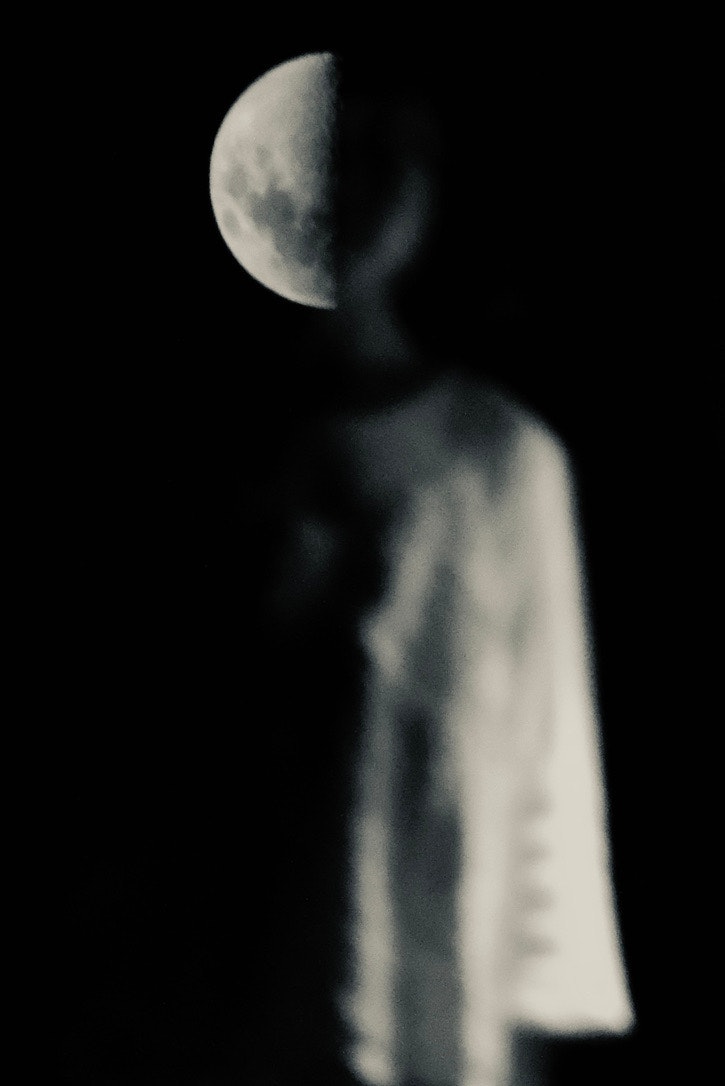 어두운 배경에 서 있는 흐릿한 인물과 반달이 보이는 모습