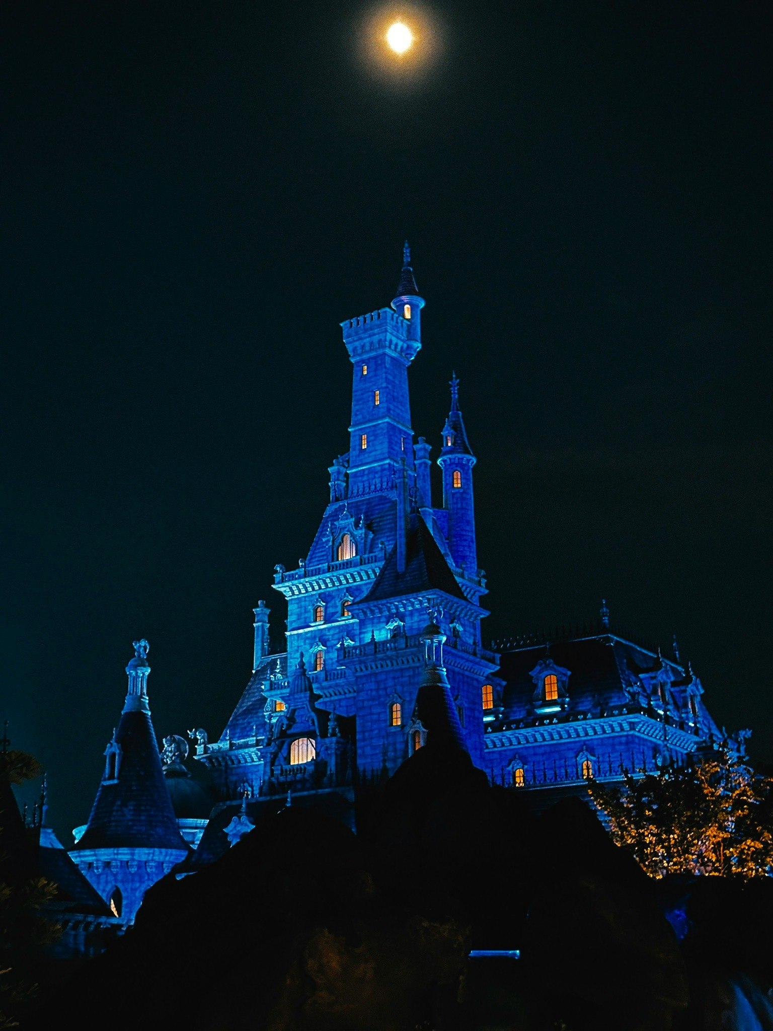 Castello illuminato di blu sotto un cielo notturno con luna piena