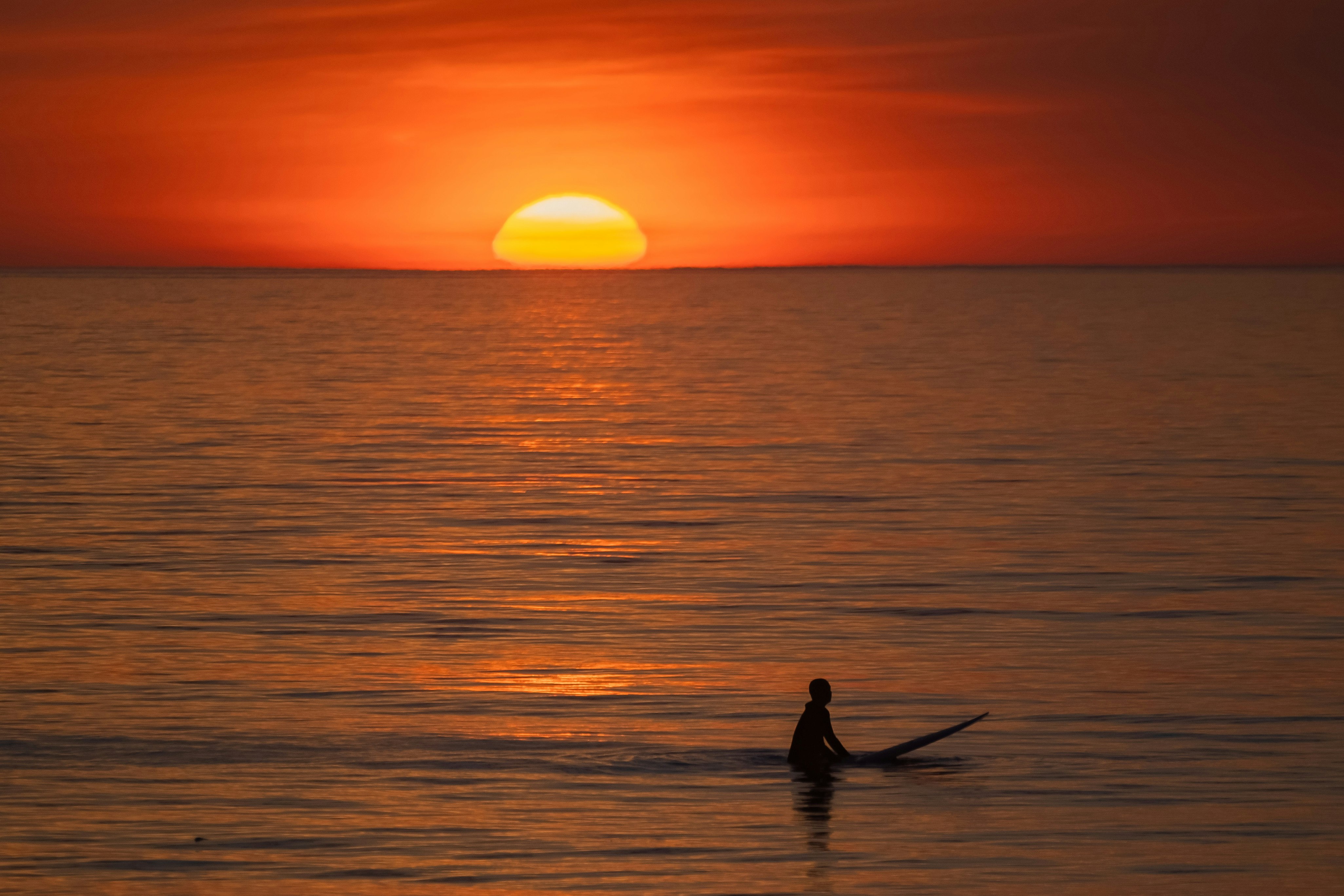 夜明けの海辺でサーフボードを持つサーファー