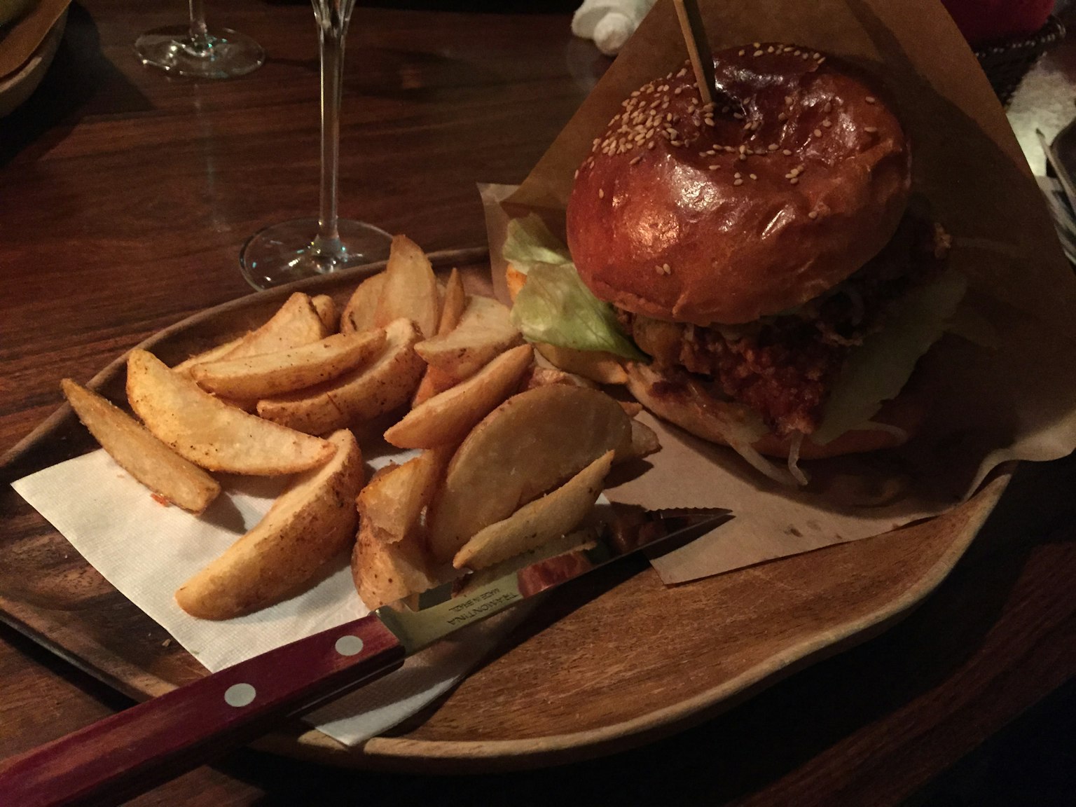 Hamburger con pane di sesamo e patatine su un piatto di legno