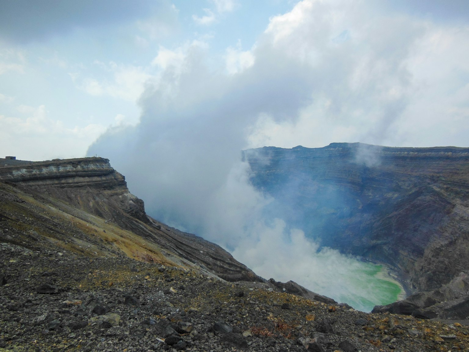 View of a volcanic crater with smoke and green water