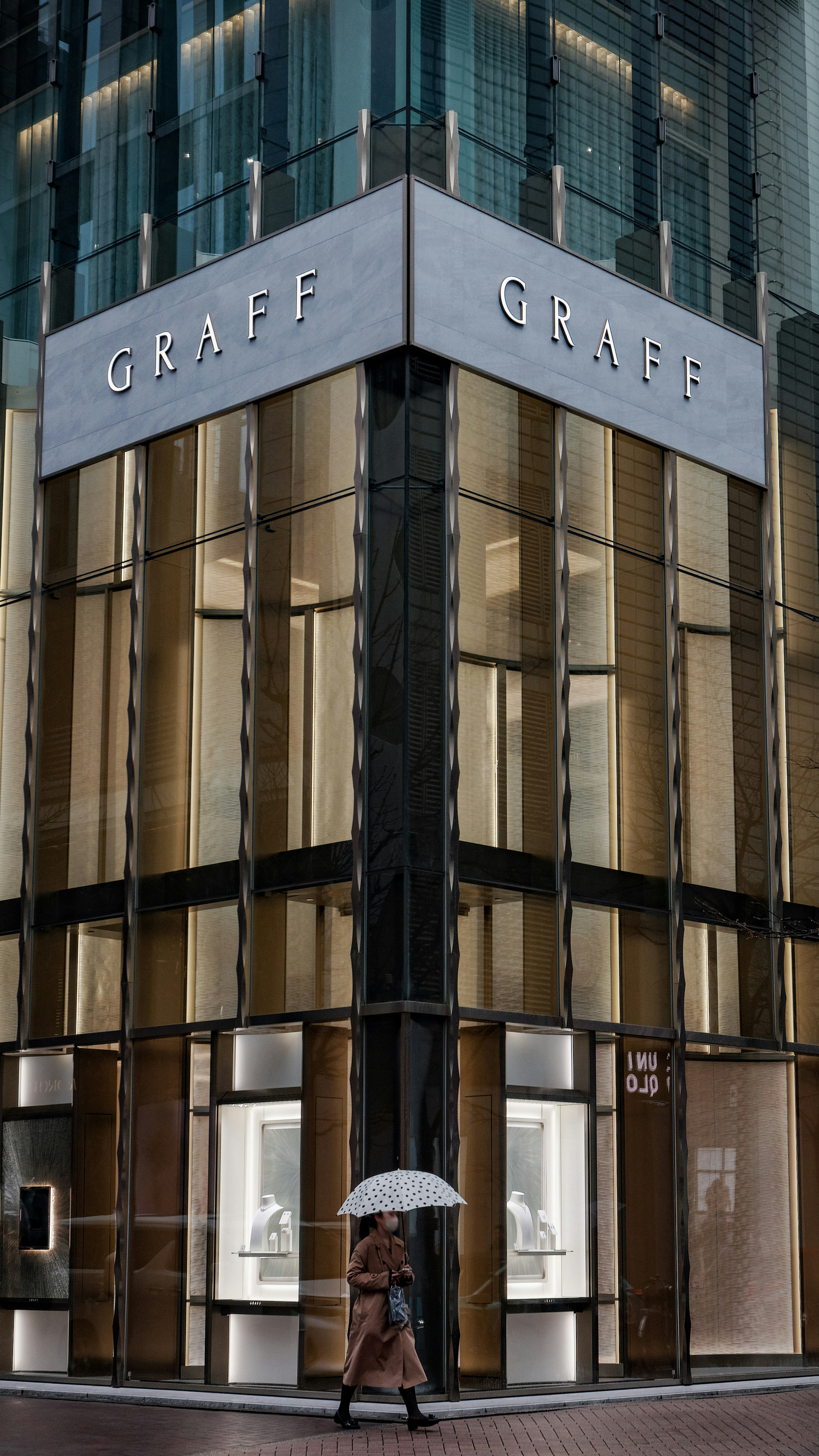 雨の銀座のビル外壁に並ぶ「GRAFF」看板と傘の人