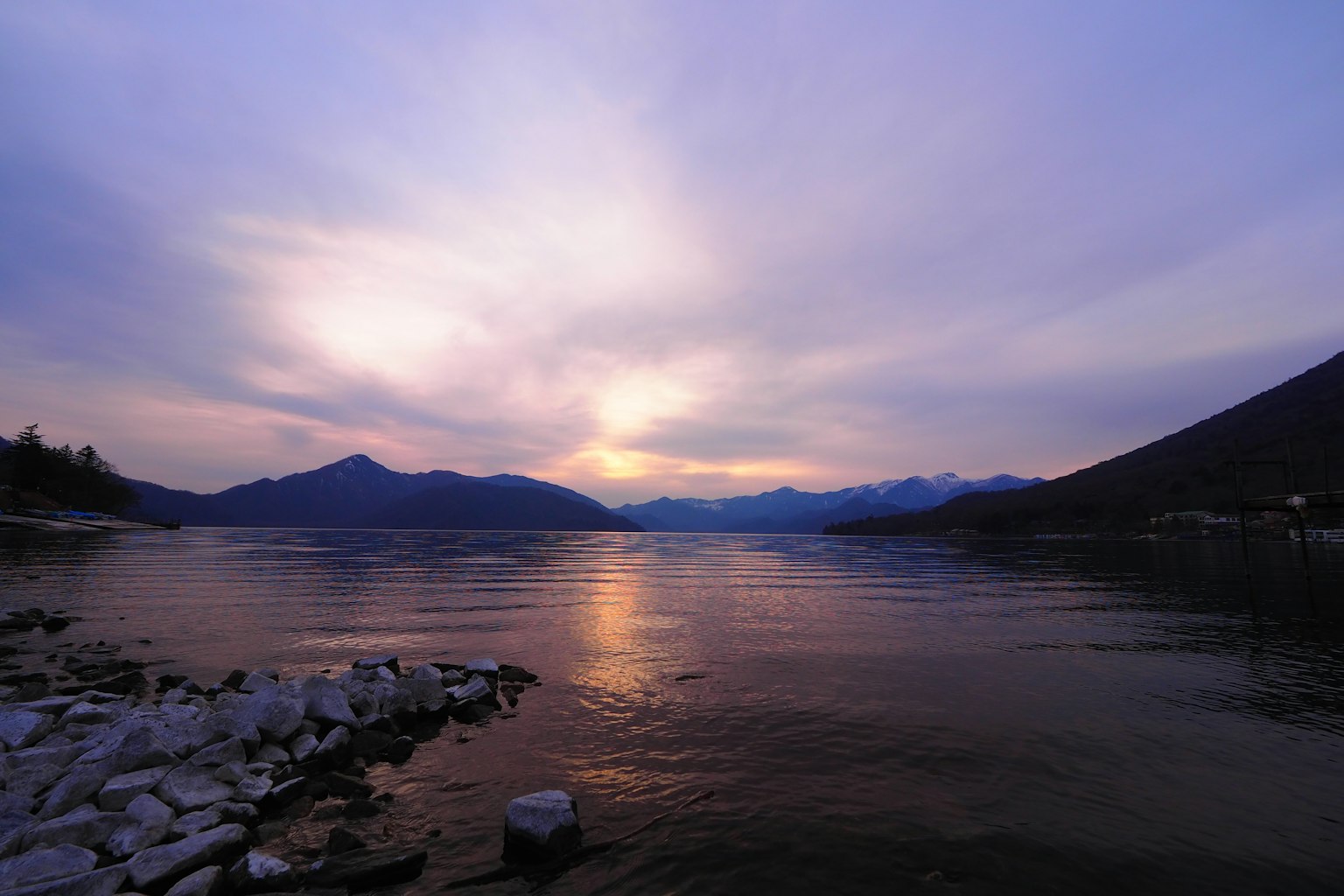 Vista tranquila de un lago al atardecer con montañas y un cielo colorido reflejado en el agua