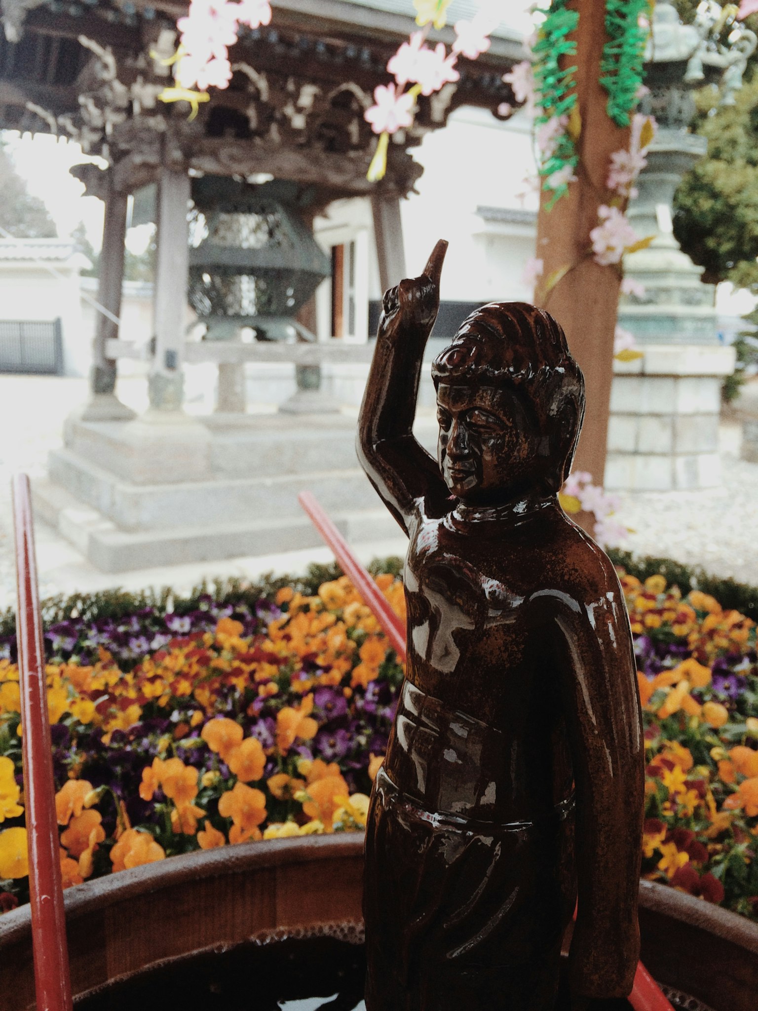 Bronze statue for pouring water surrounded by colorful flowers in a temple setting