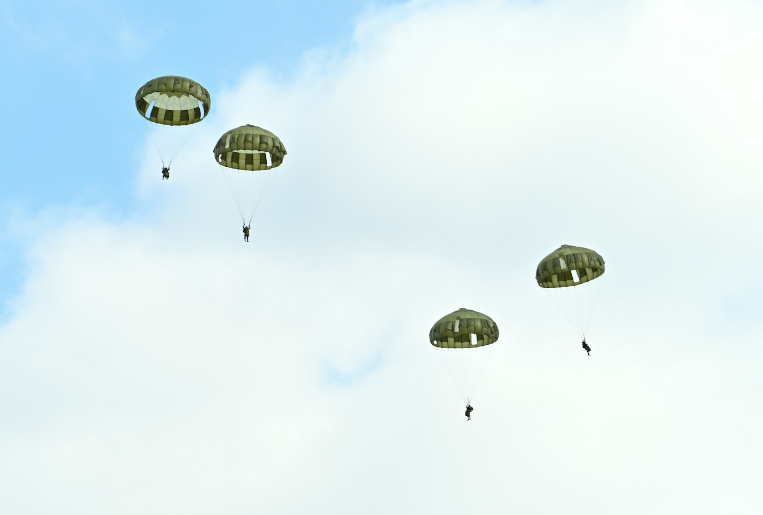 Parachutistes descendant avec des parachutes verts dans un ciel nuageux