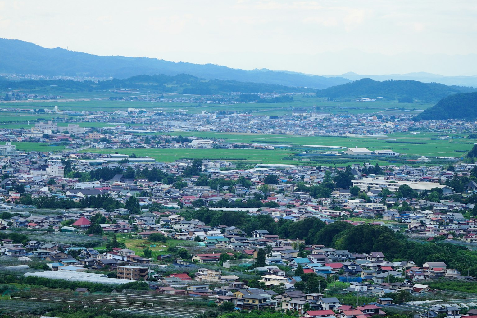 被郁郁葱葱的山脉环绕的小镇全景，拥有众多房屋和田地
