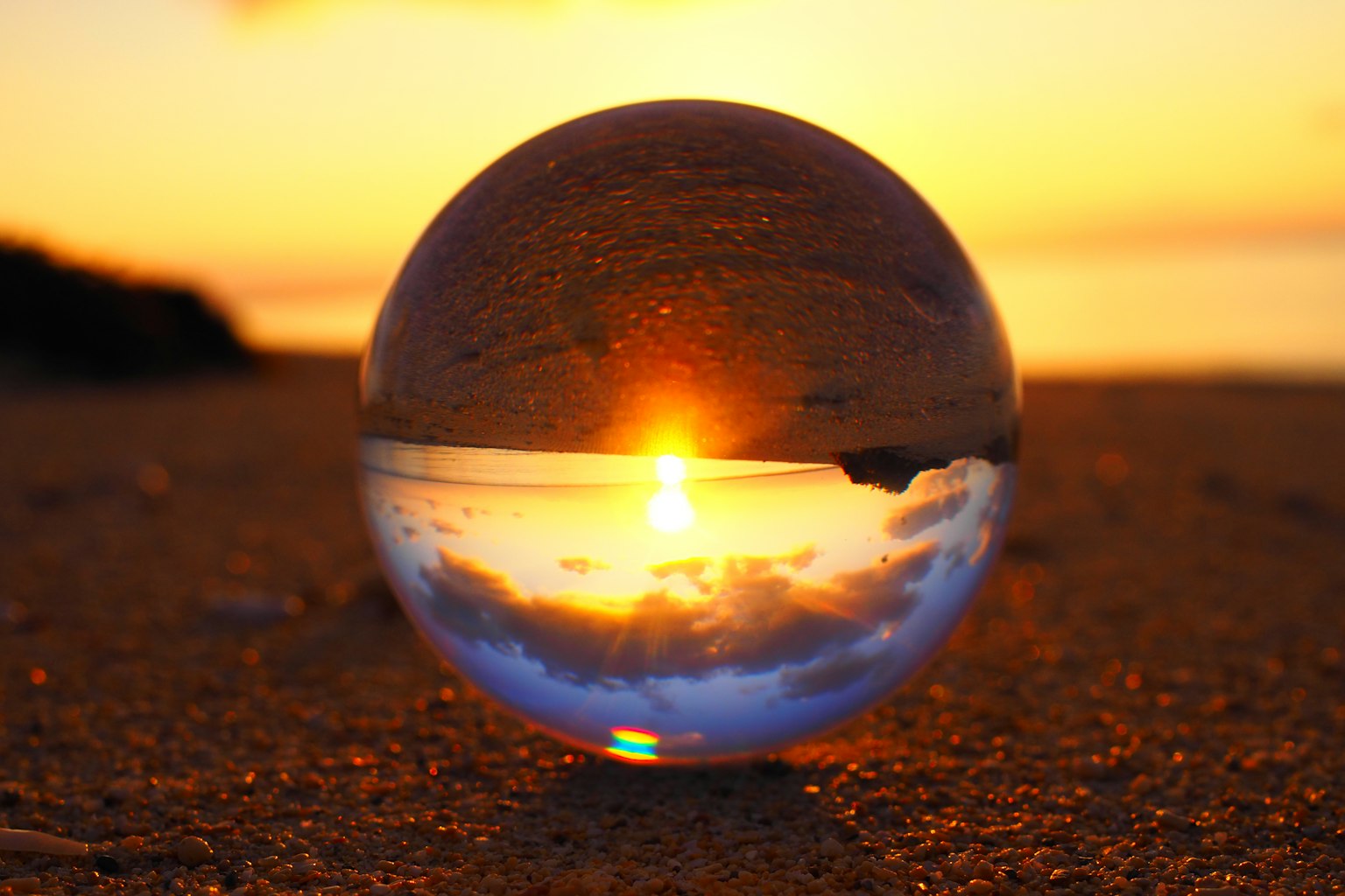 Crystal ball reflecting sunset and surrounding sandy beach