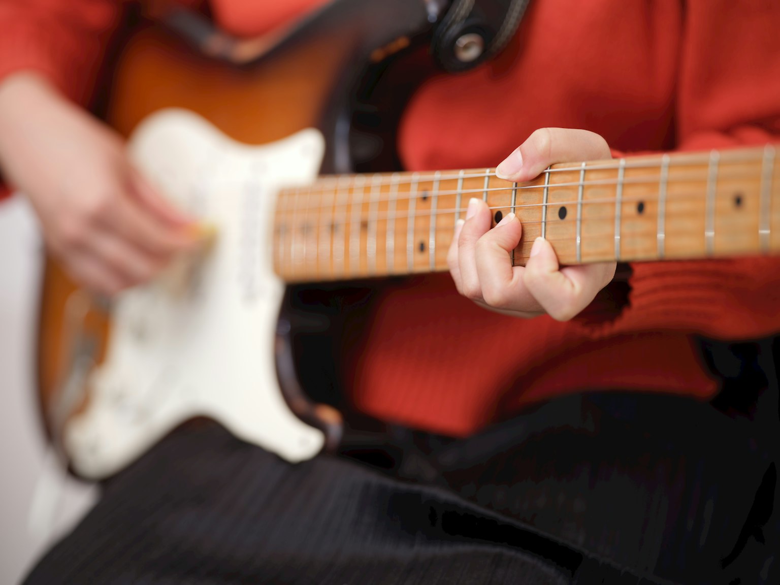 Close-up of a person playing an electric guitar wearing an orange sweater with a brown and white guitar