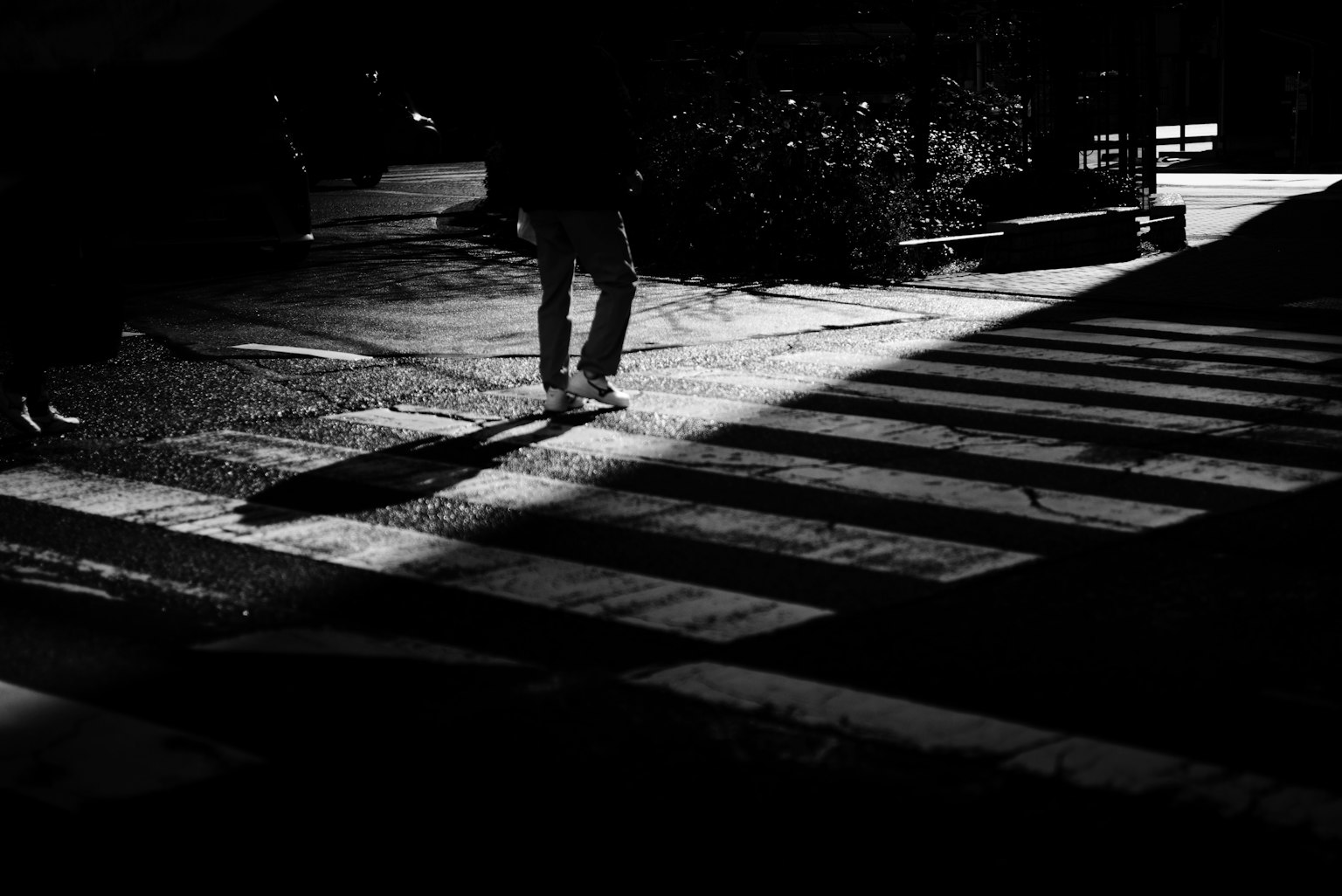 Una persona cruzando un paso de peatones con sombras y luz contrastante