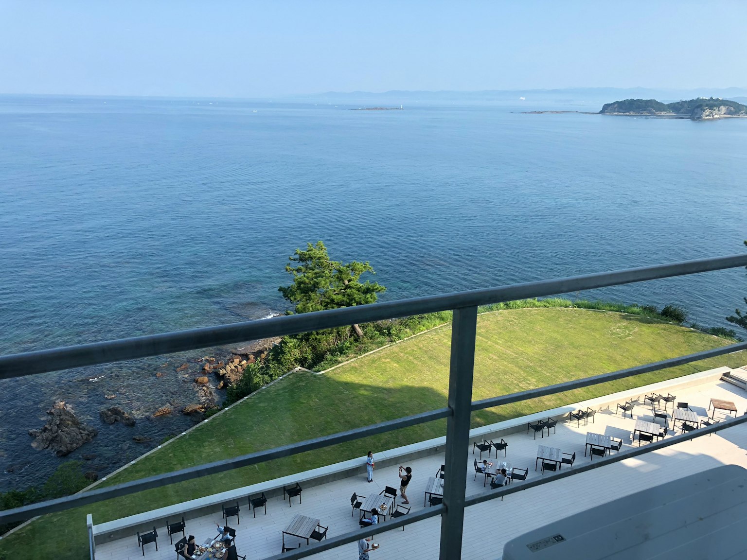 Balcony view featuring blue ocean and bright sky with grassy area and sun loungers along the coastline