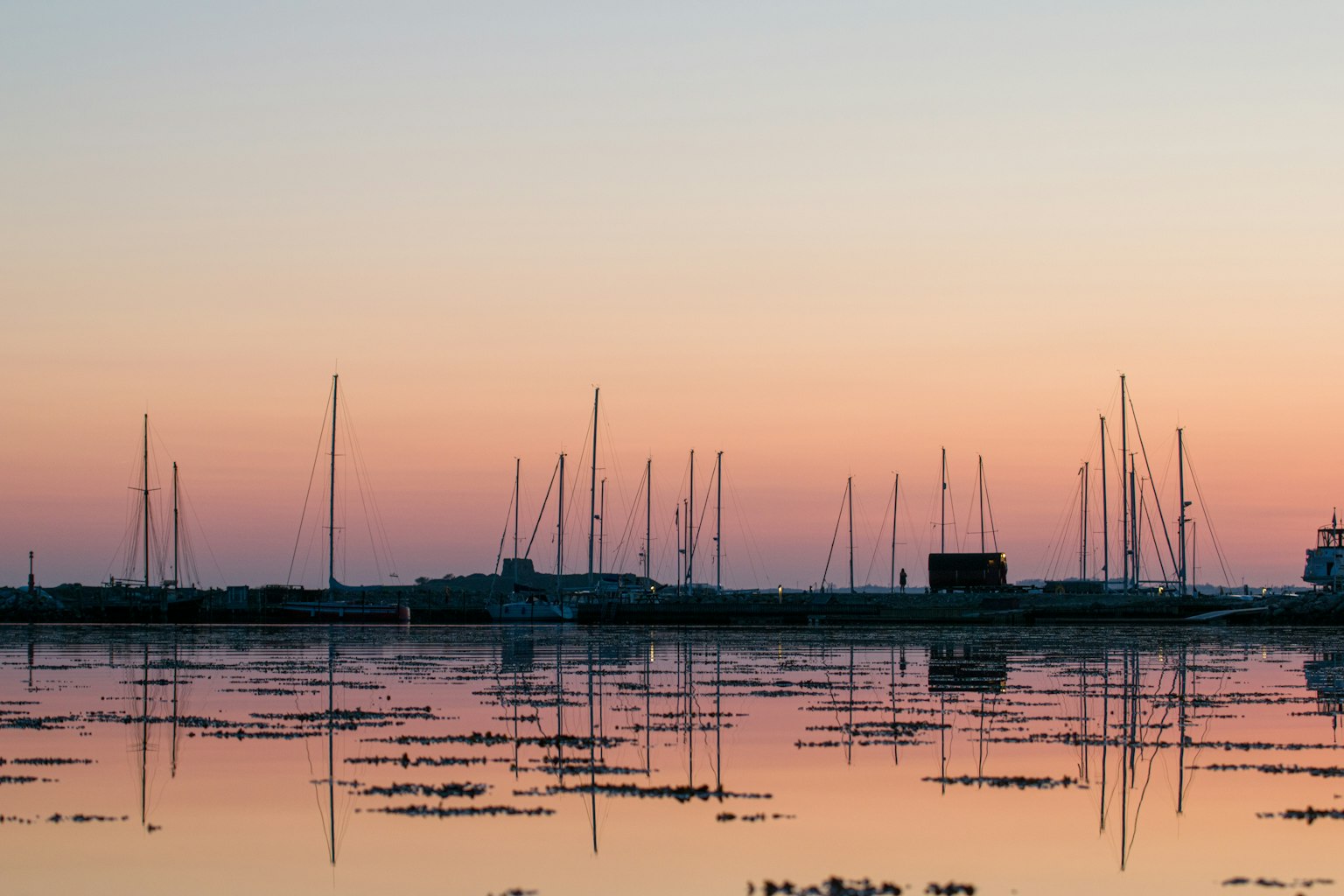 Silhouetted yacht masts against a sunset sky with reflections in water