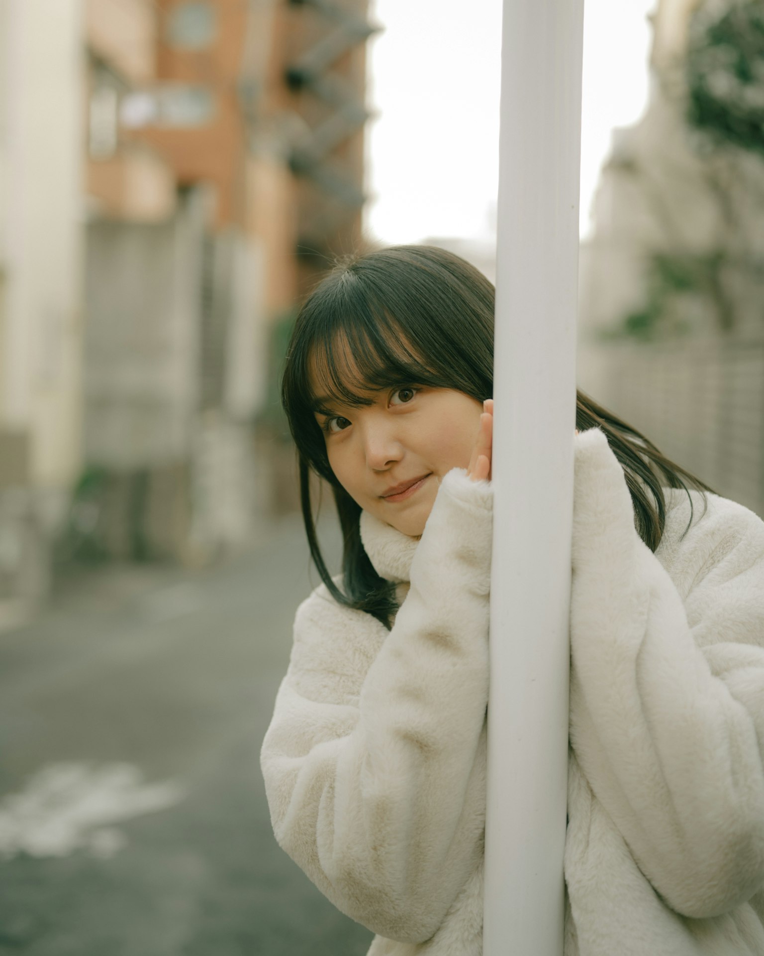 穿着白色外套的女性靠在城市街道上的一根柱子上