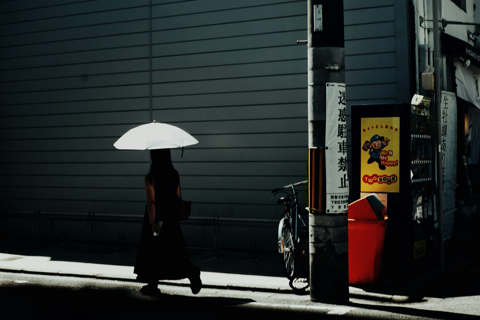 白い傘を持った女性が影の中を歩いている街の風景