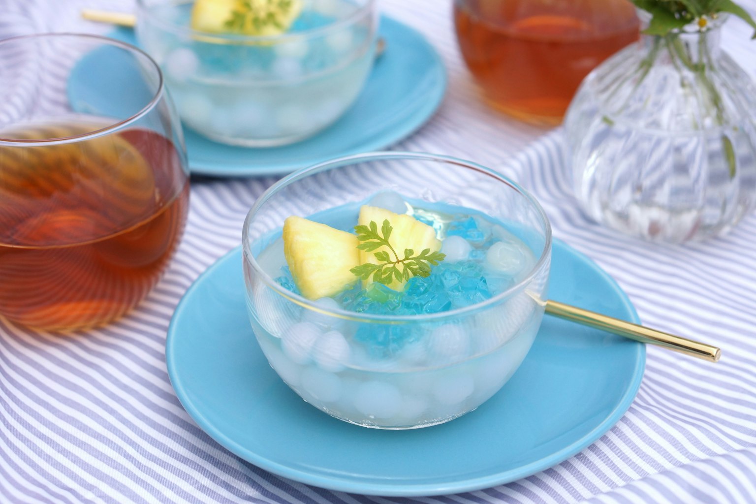 Hình ảnh của món tráng miệng trong bát trong suốt với thạch xanh và đá lạnh, trang trí bằng lát dứa và một chiếc lá