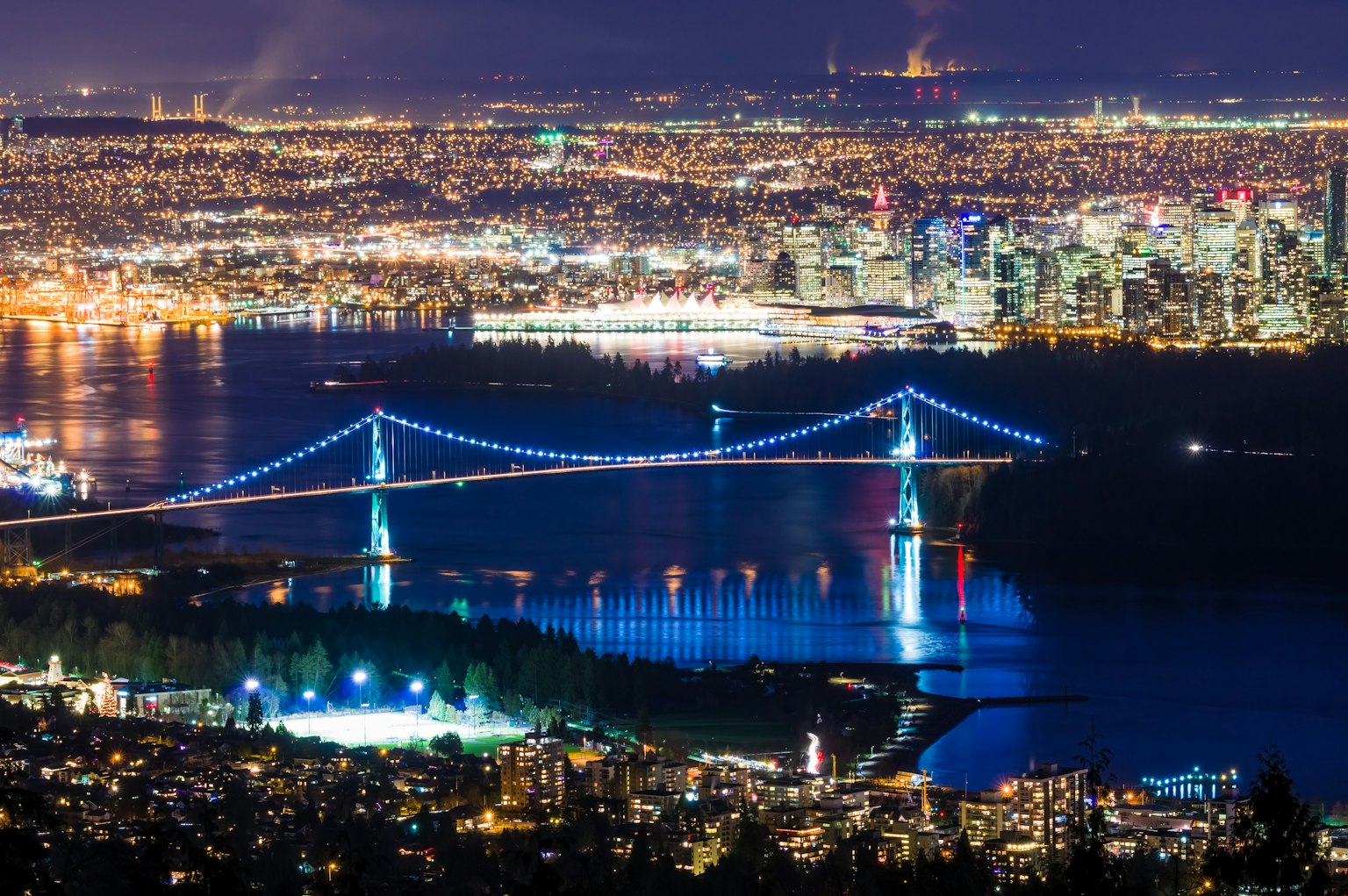 Vista nocturna de Vancouver mostrando el puente Lions Gate iluminado con luces azules