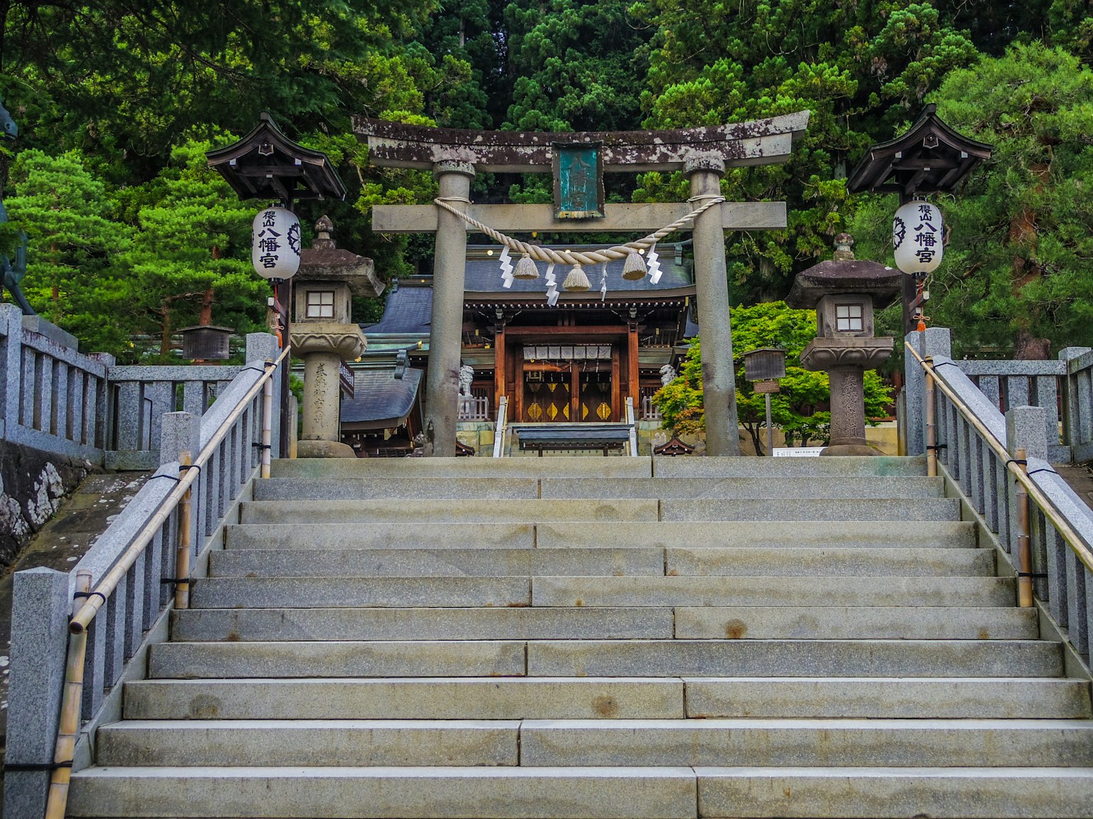 Escalones de piedra que llevan a un santuario con un torii y faroles