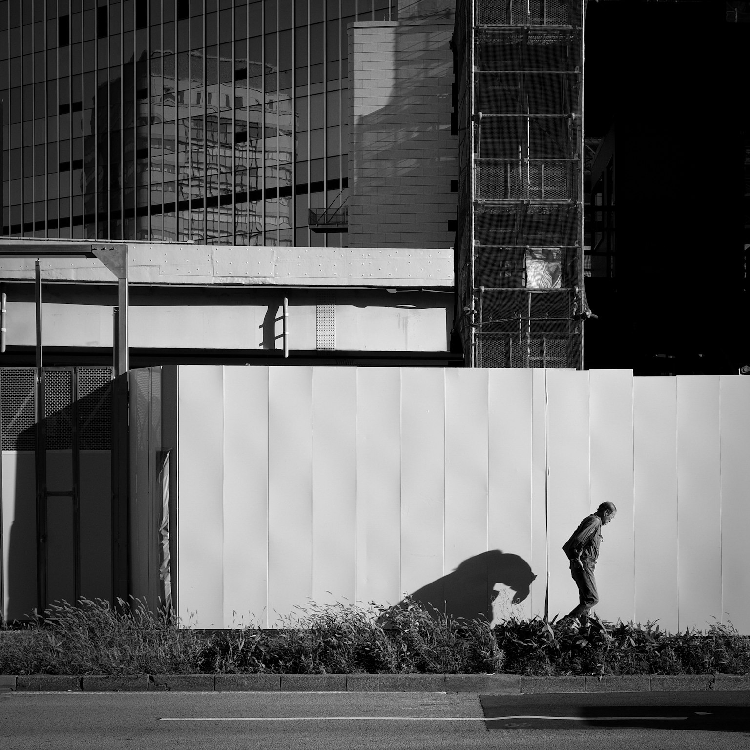 Black and white urban scene with a walking man and his shadow on a building wall