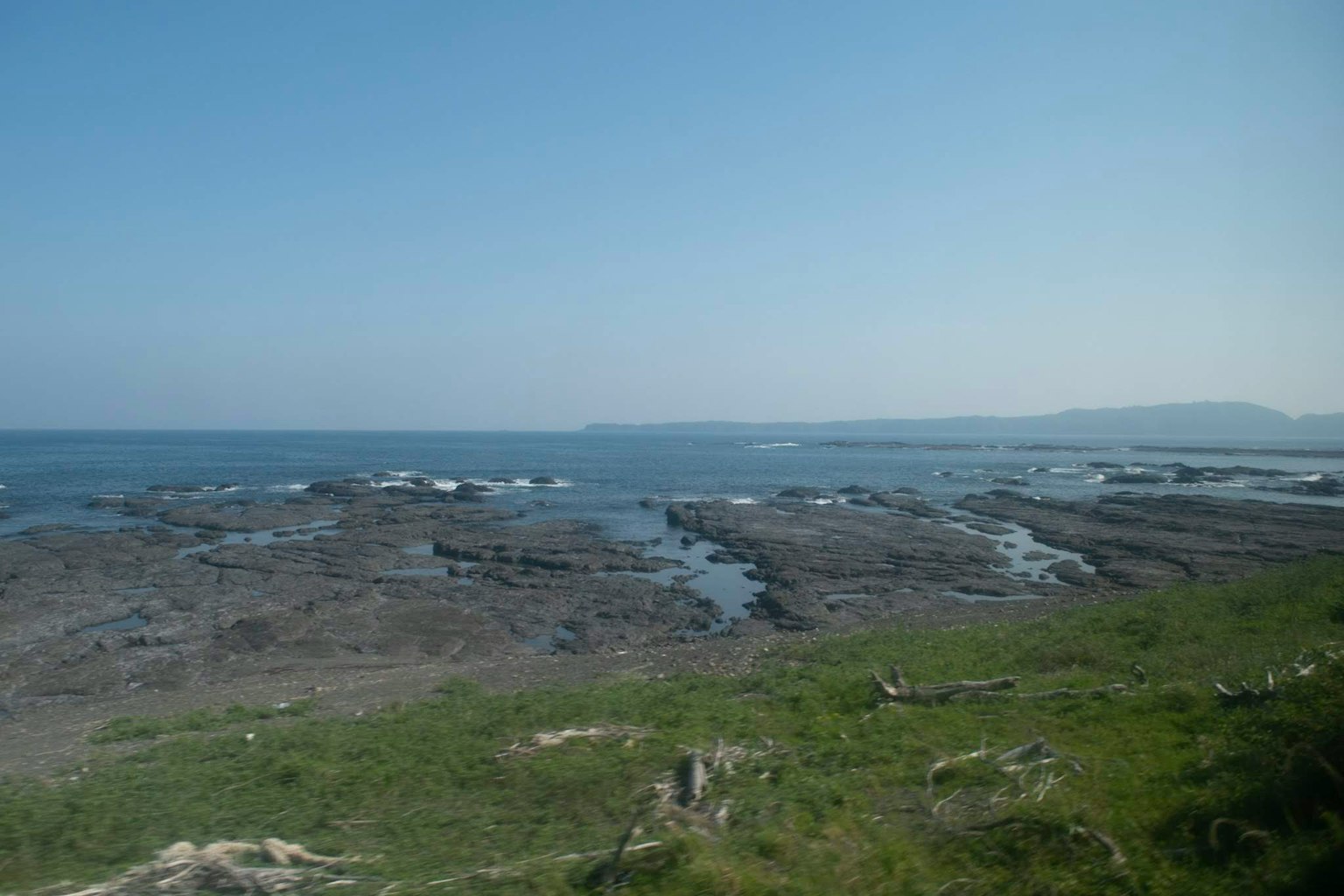 Scenic view of the sea with rocky shore and green grass under a clear blue sky