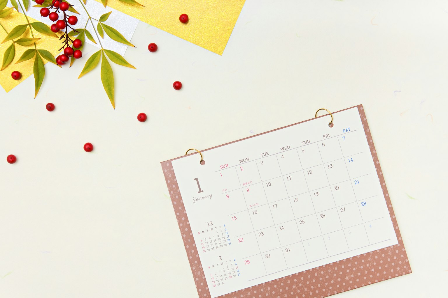 Un calendario sobre una mesa rodeado de bayas rojas y hojas verdes