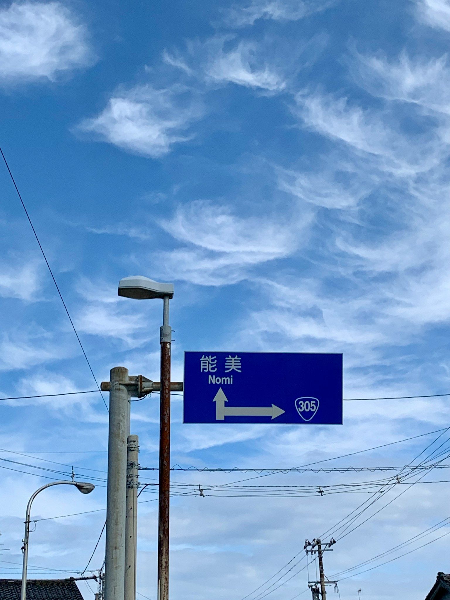 Cartello stradale direzionale con sfondo blu e lampione sotto un cielo sereno