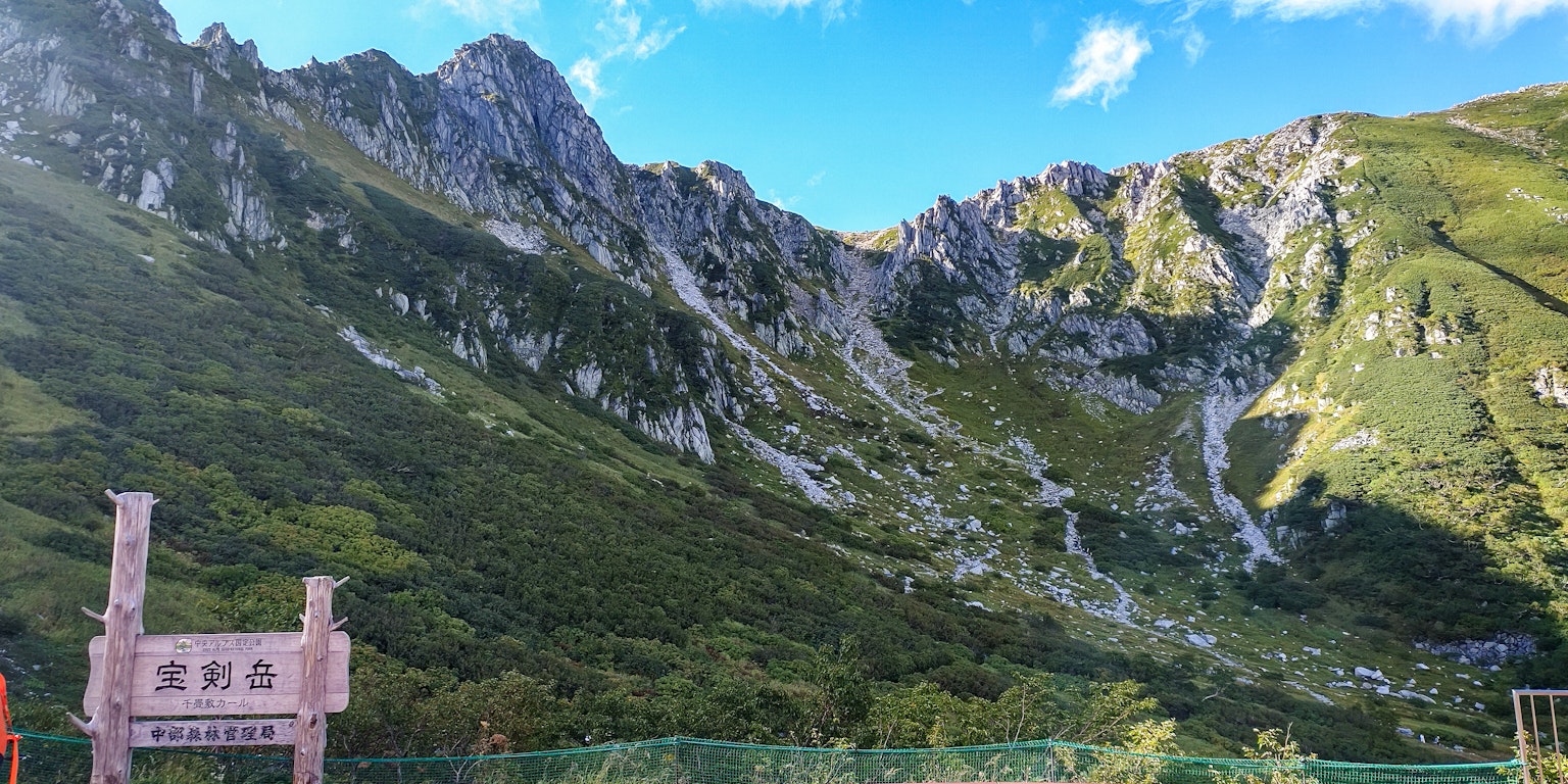 Vista panoramica di montagne sotto un cielo blu con un cartello in primo piano