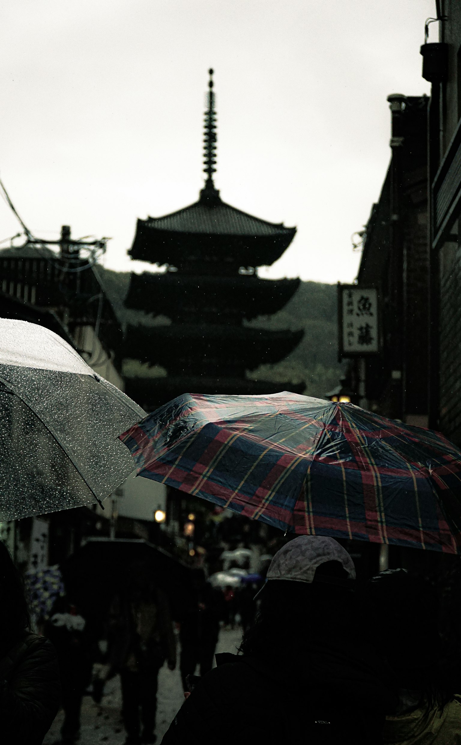People with umbrellas in the rain near a pagoda