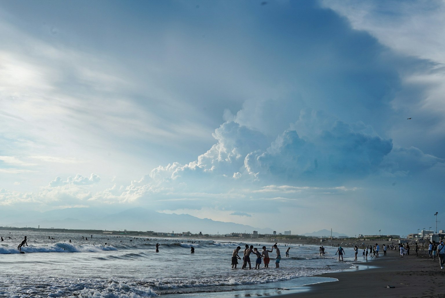 Scene of people playing in the ocean under a blue sky with clouds