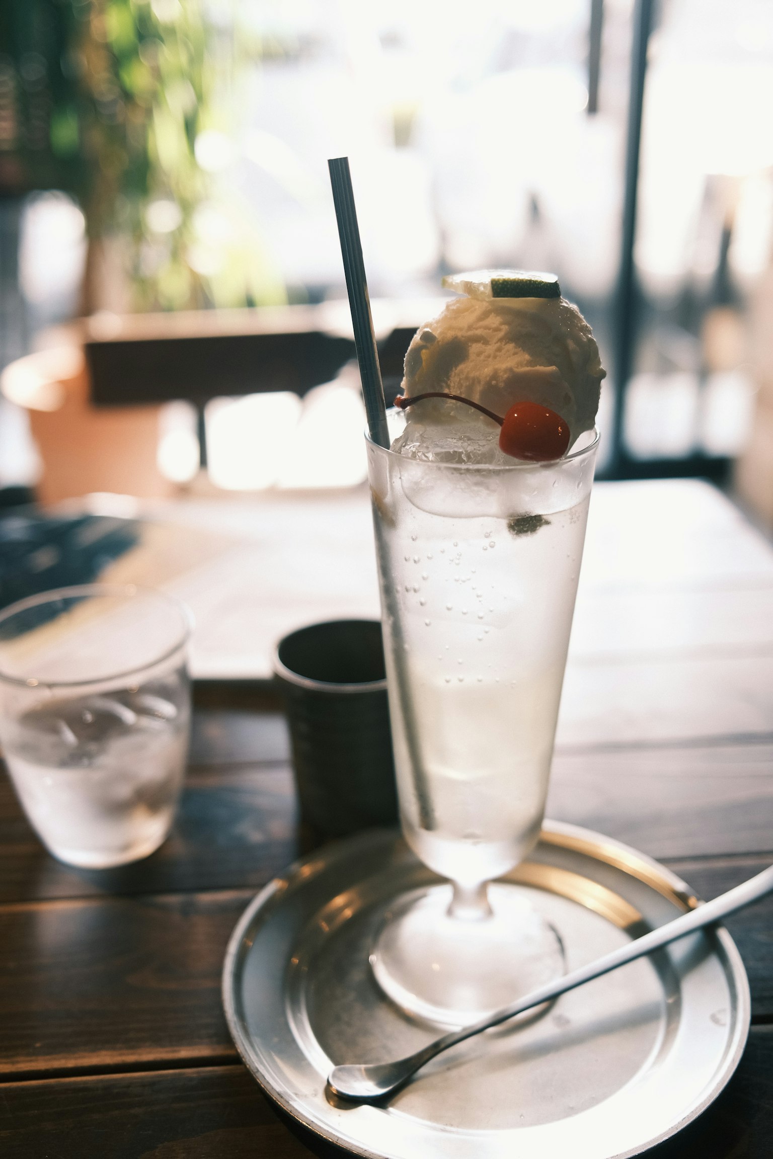 Gelas tinggi berisi minuman bening dan es, dihias dengan sedotan dan ceri