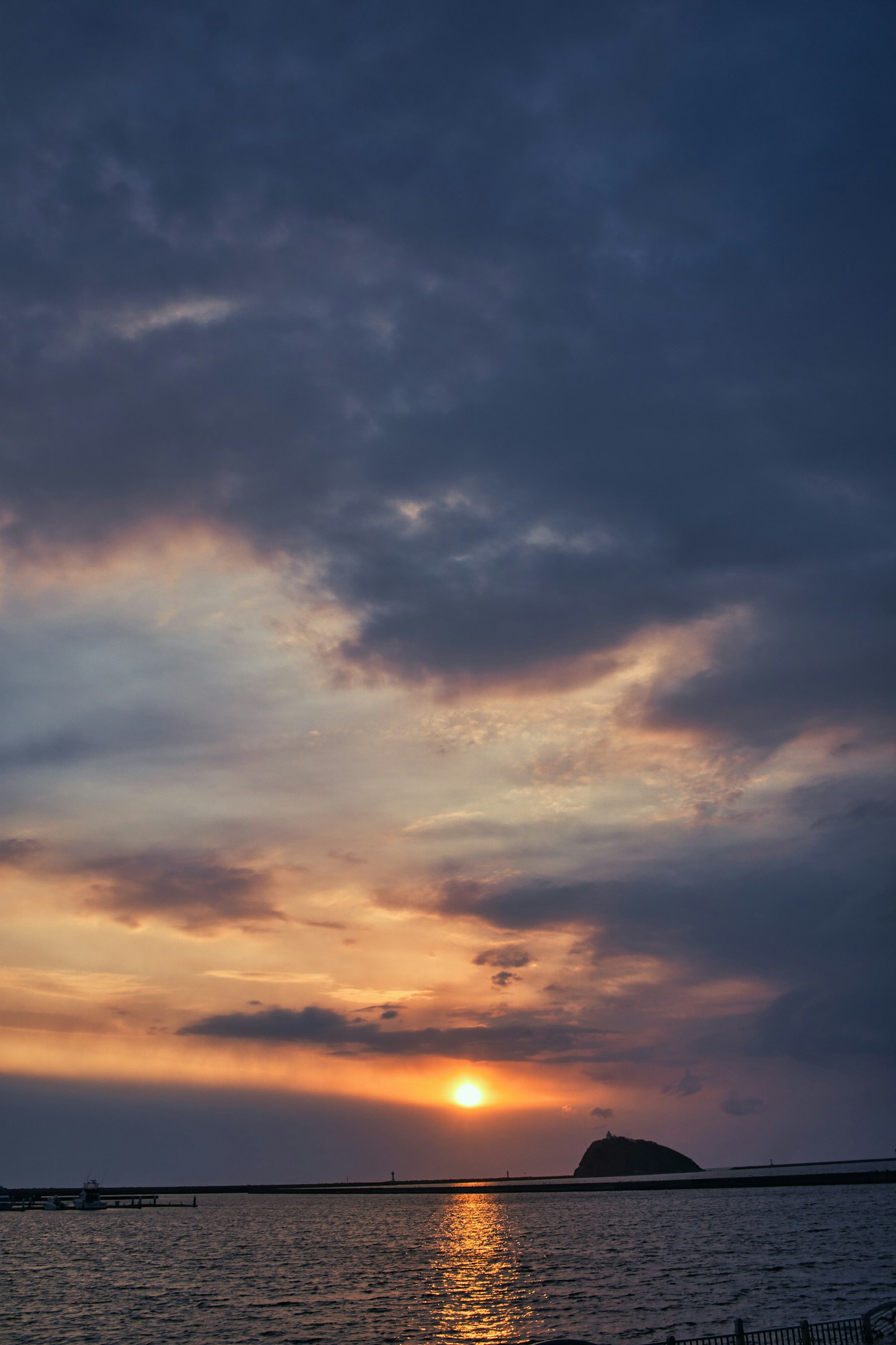 Coucher de soleil sur la mer avec des nuages et une formation rocheuse au loin