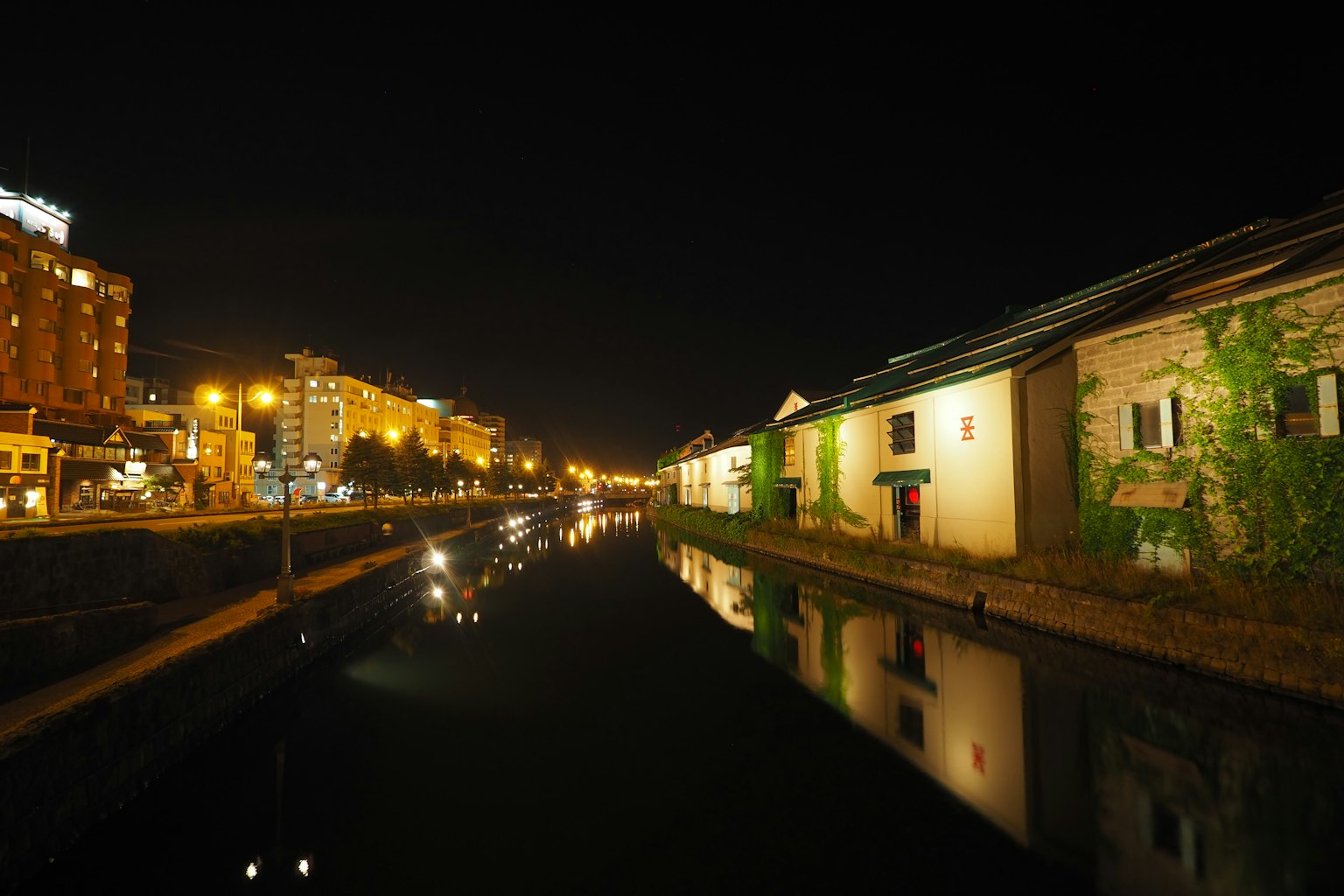 Vista nocturna de edificios a lo largo de un canal con reflejos y farolas