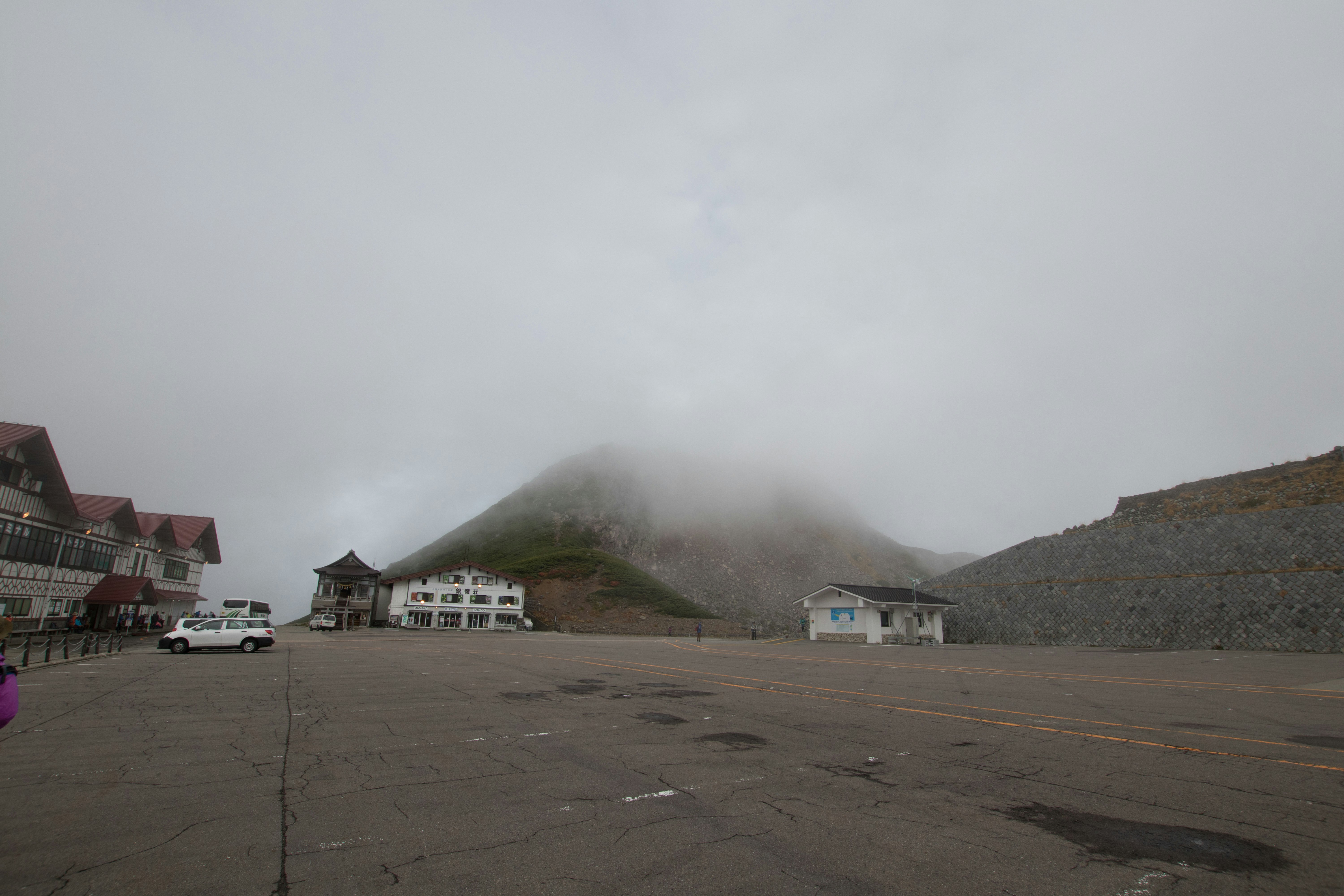 霧に包まれた山の麓の広い駐車場と建物