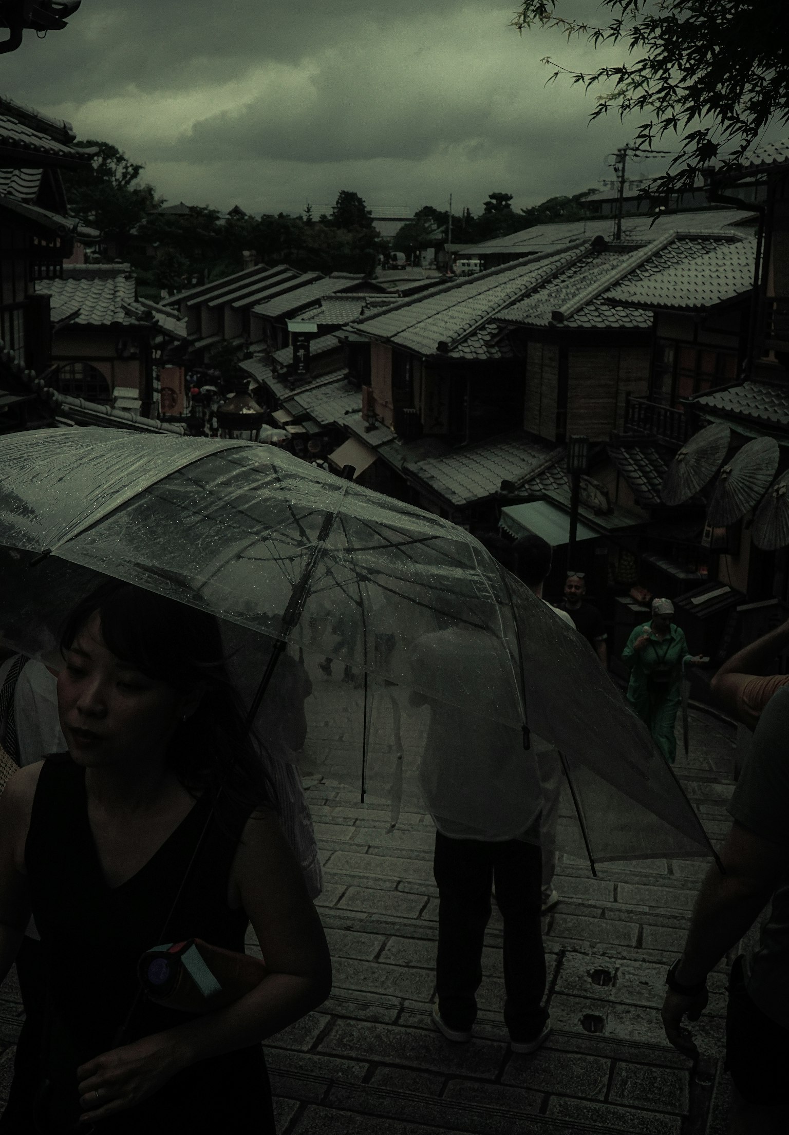 Personas caminando bajo la lluvia con paraguas en una escena nublada de Kioto