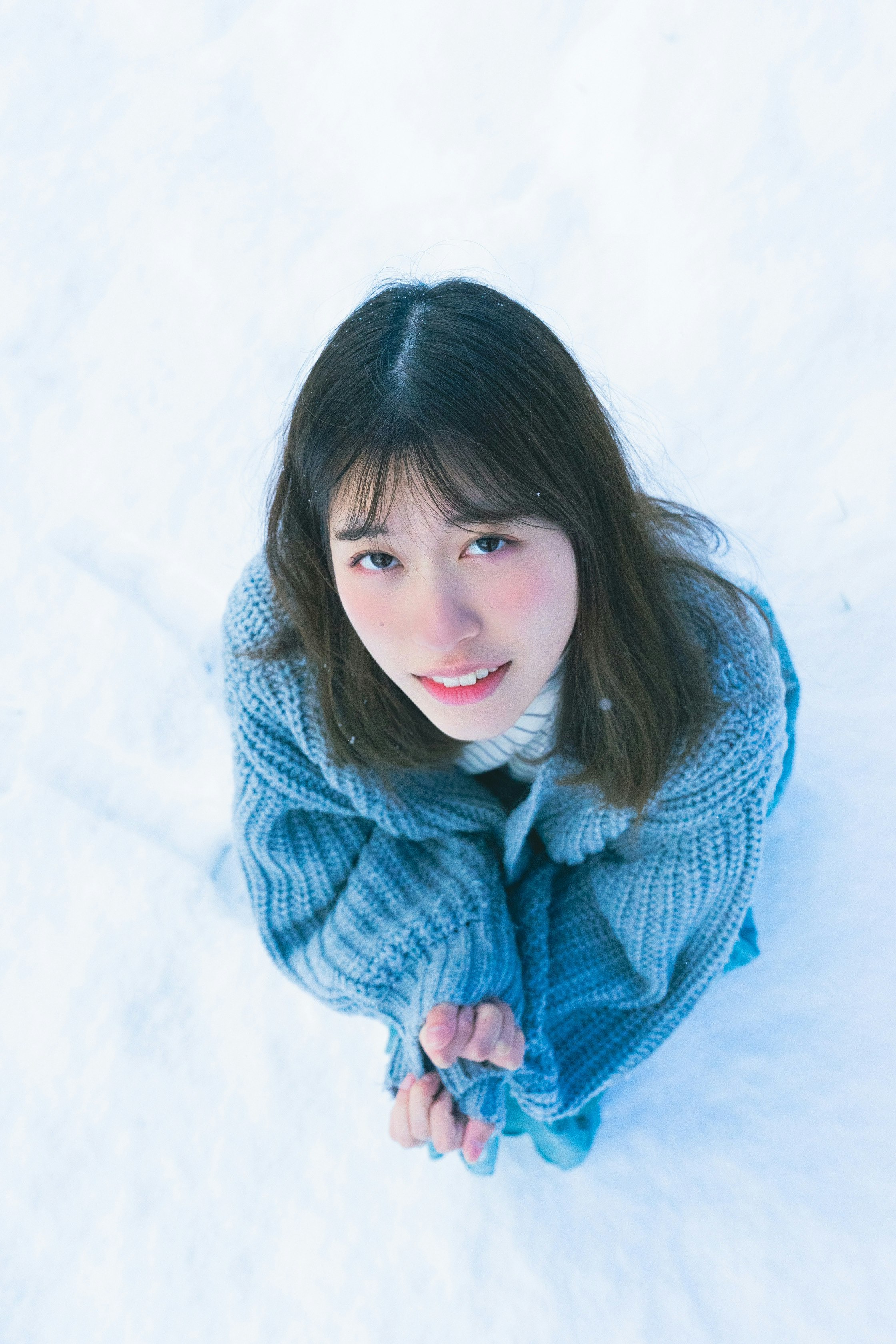woman in a knit sweater reaching toward the camera against a snowy white background
