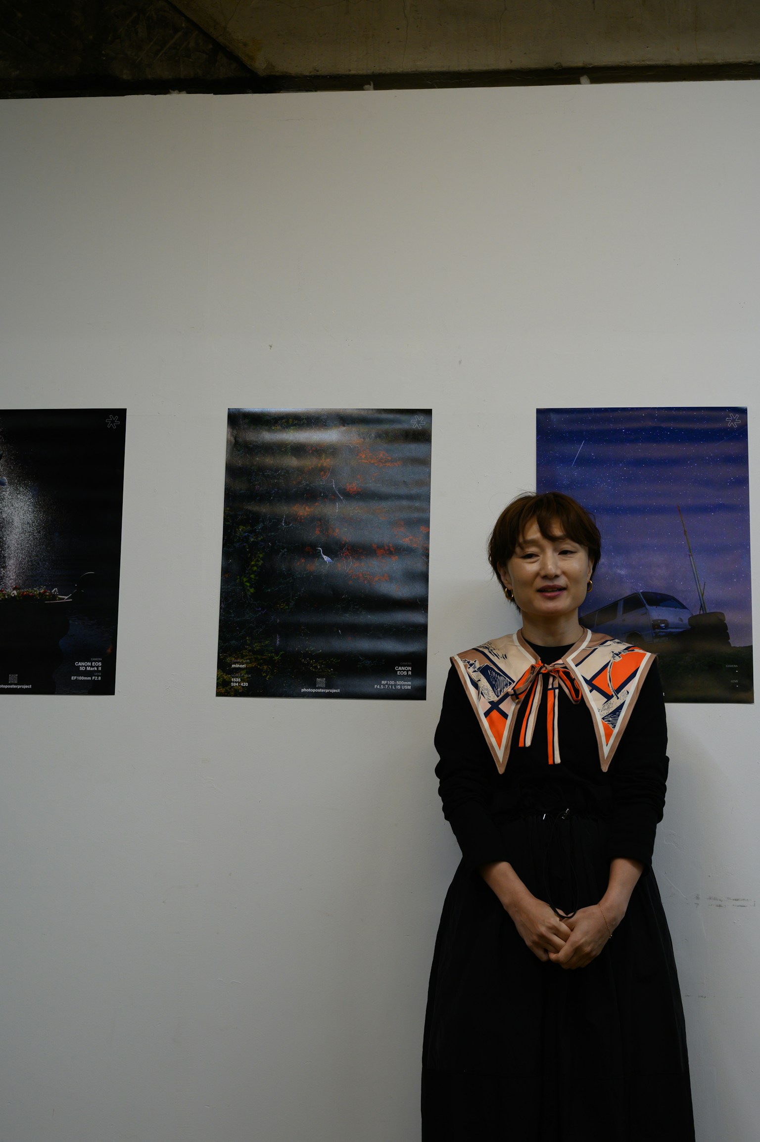 展览中站在海报前的女性照片 穿着黑色连衣裙和橙色丝带领子