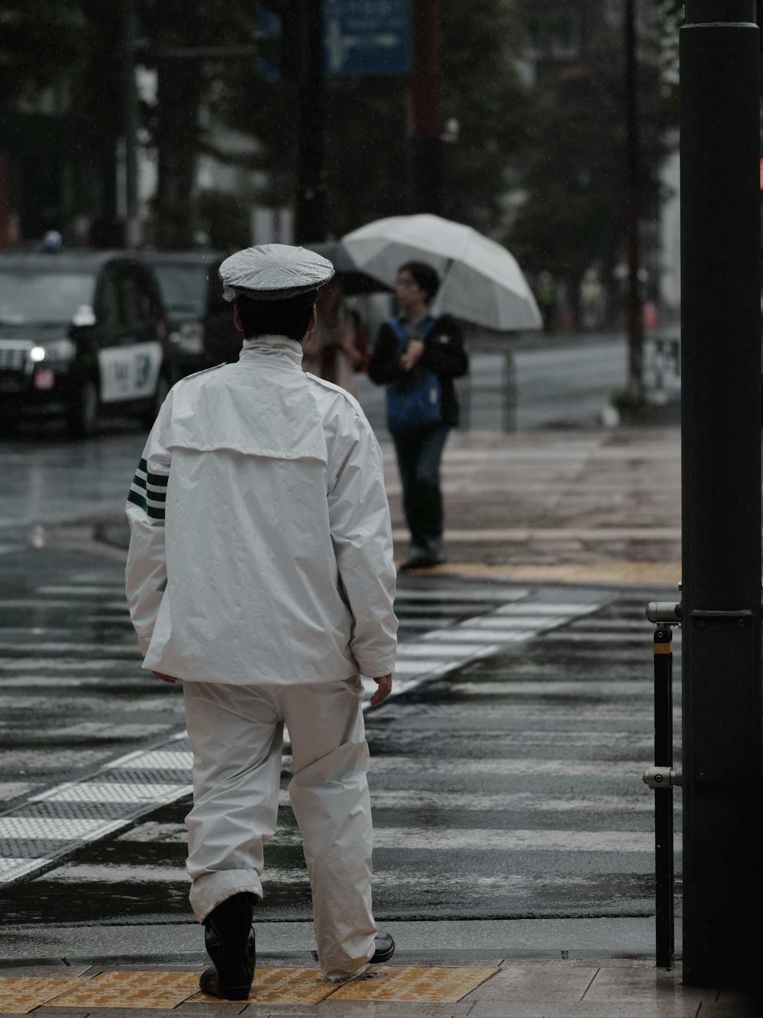 Un policier en uniforme blanc marchant sous la pluie avec des personnes tenant des parapluies