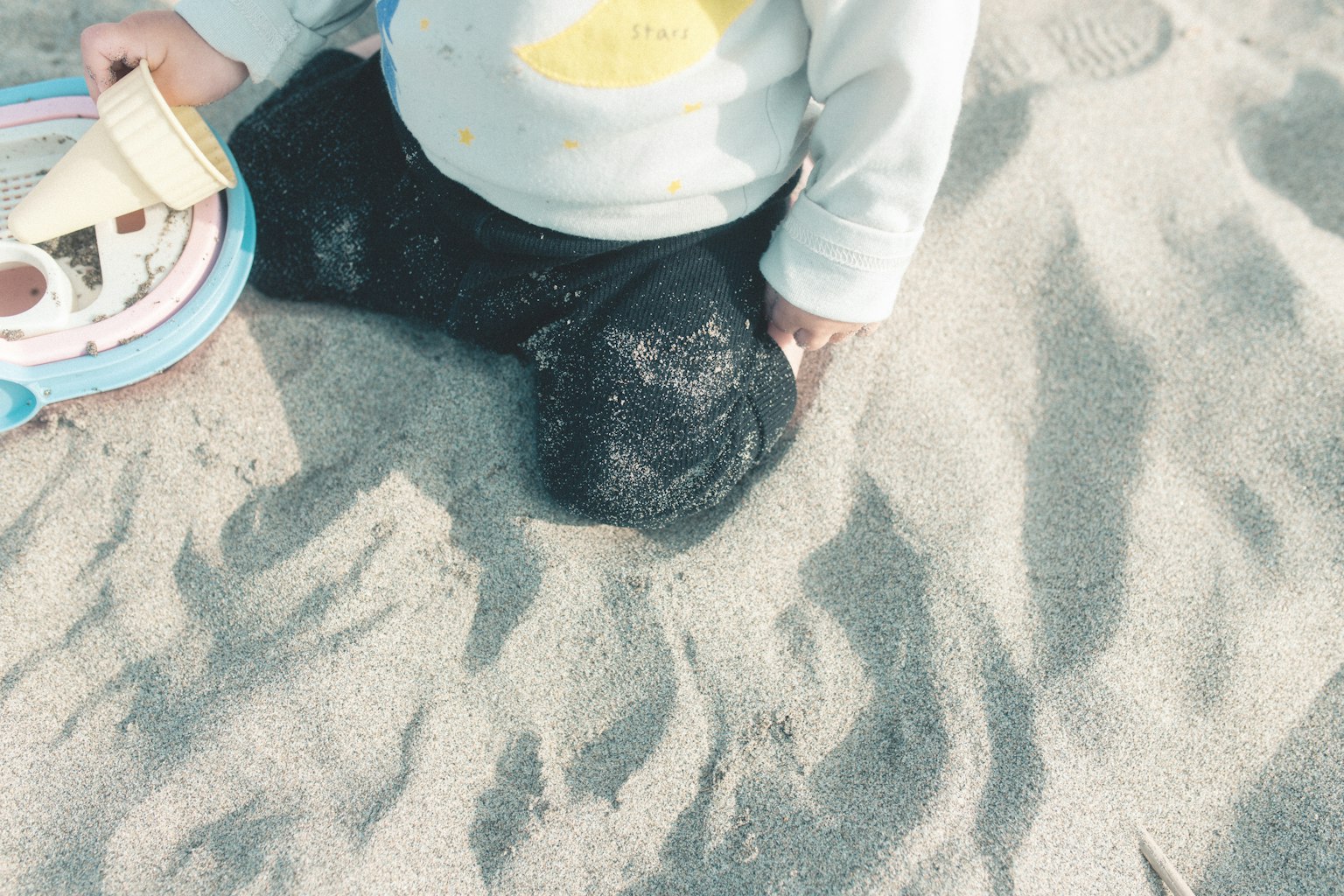 Kind sitzt im Sand mit einem Spielzeug