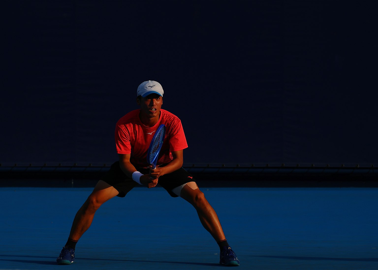 Un hombre con camiseta roja está en posición en una cancha de tenis