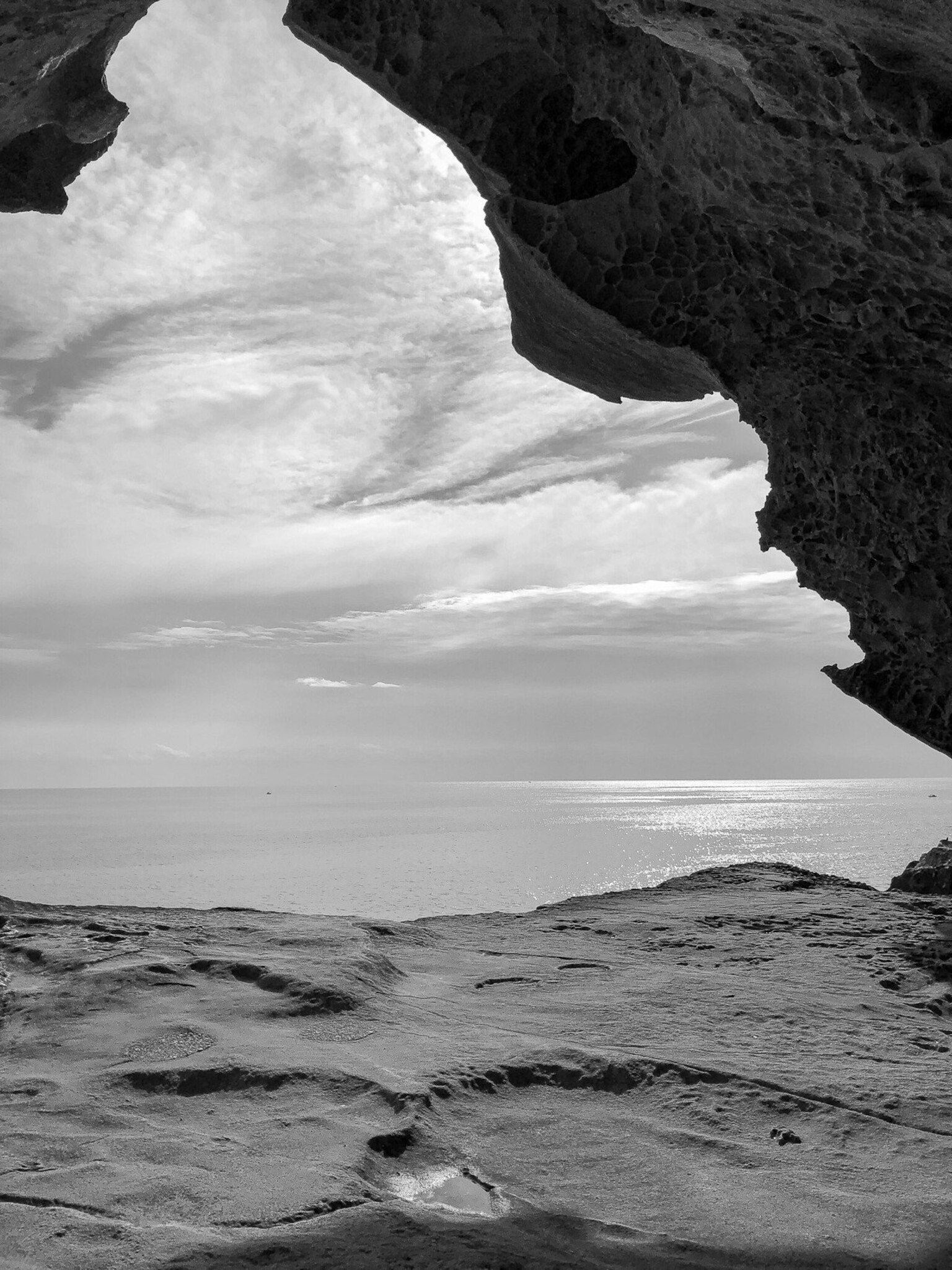 Imagen en blanco y negro de una cueva de roca con el océano y el cielo de fondo