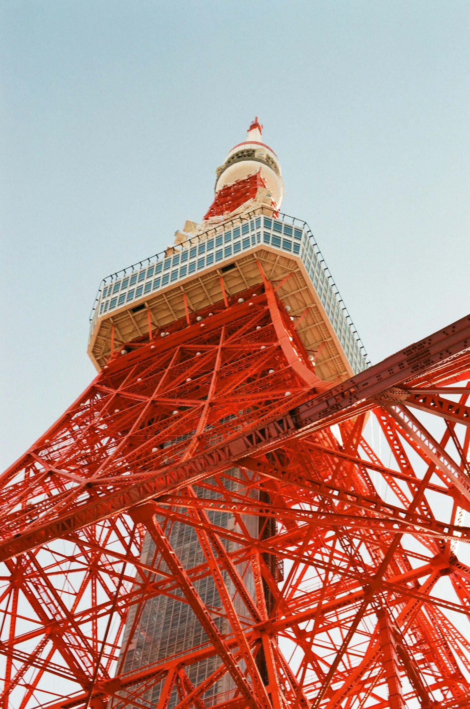 Blick nach oben auf den Tokyo Tower mit seiner roten Stahlkonstruktion vor blauem Himmel