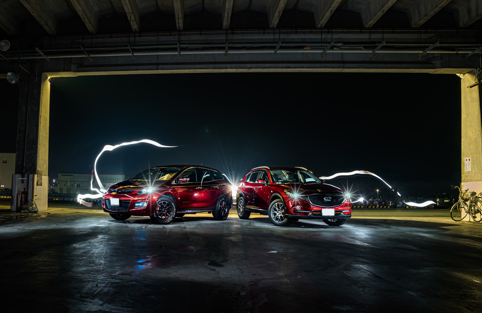 Two red cars parked indoors at night with light trails