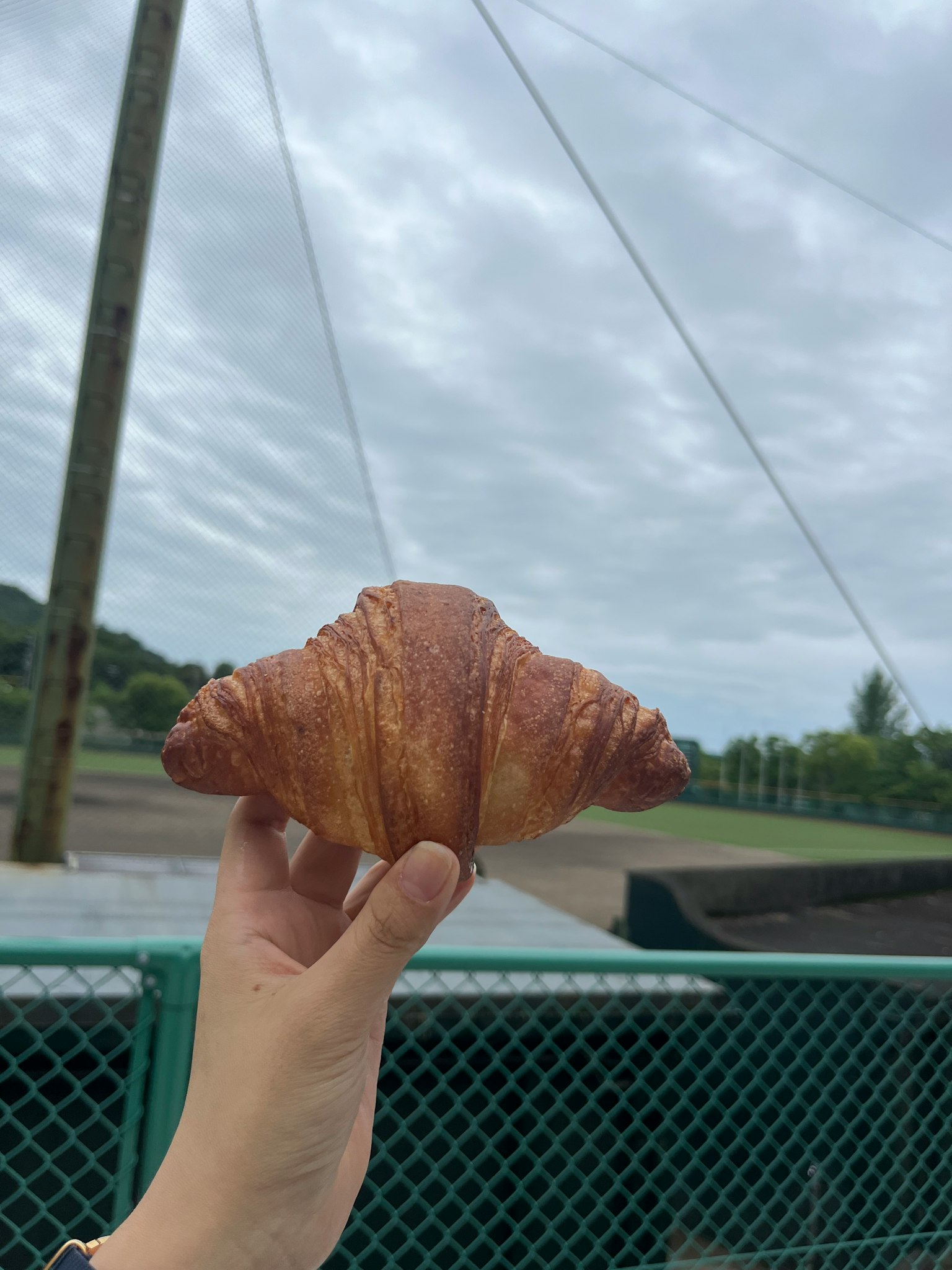 Sebuah tangan memegang croissant di bawah langit mendung