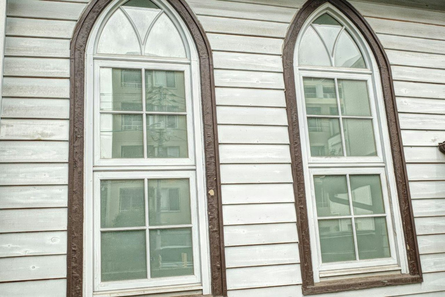 Two arched windows on a wooden wall with white paint