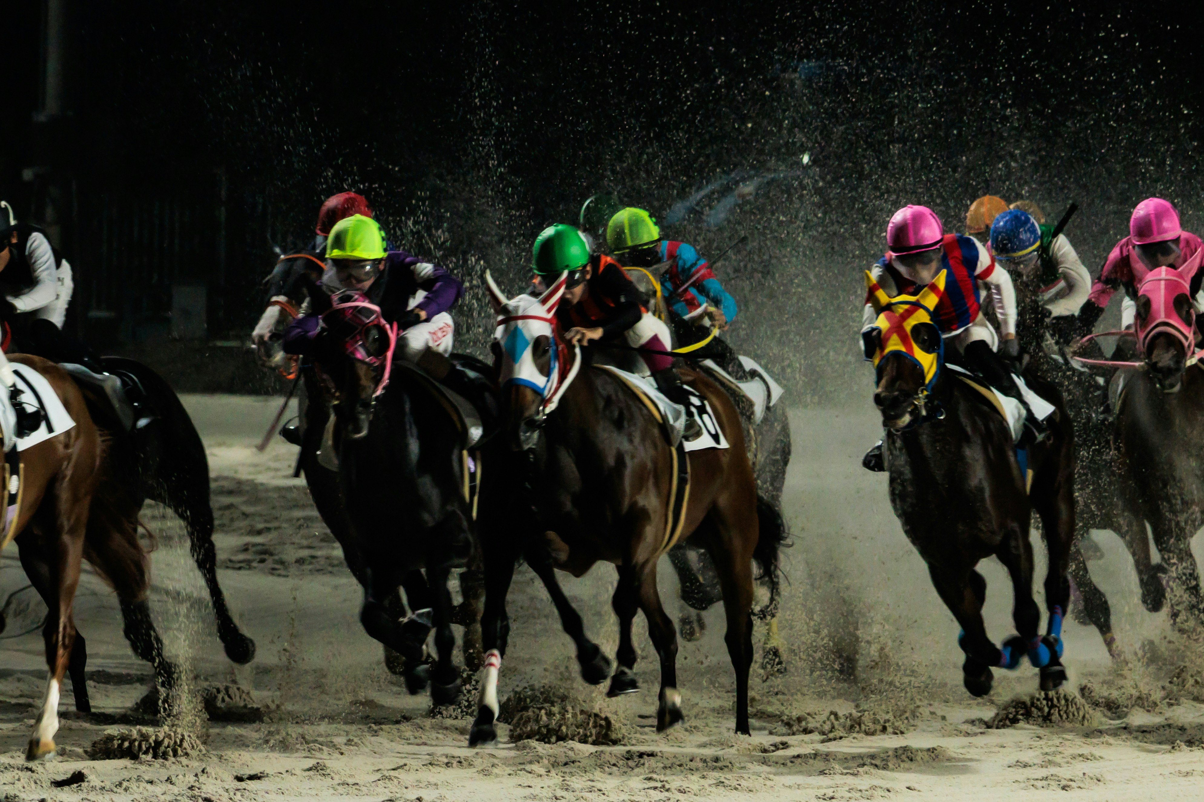 夜の競馬場を走る騎手と馬の集団