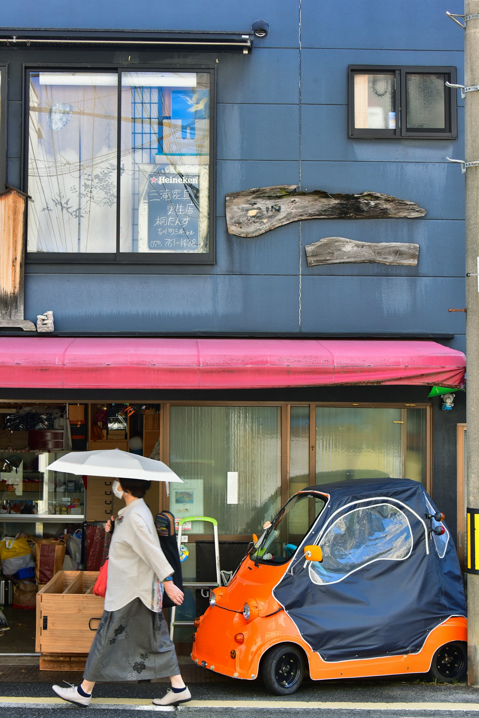 青い壁の前を歩く女性とオレンジ色の小型車
