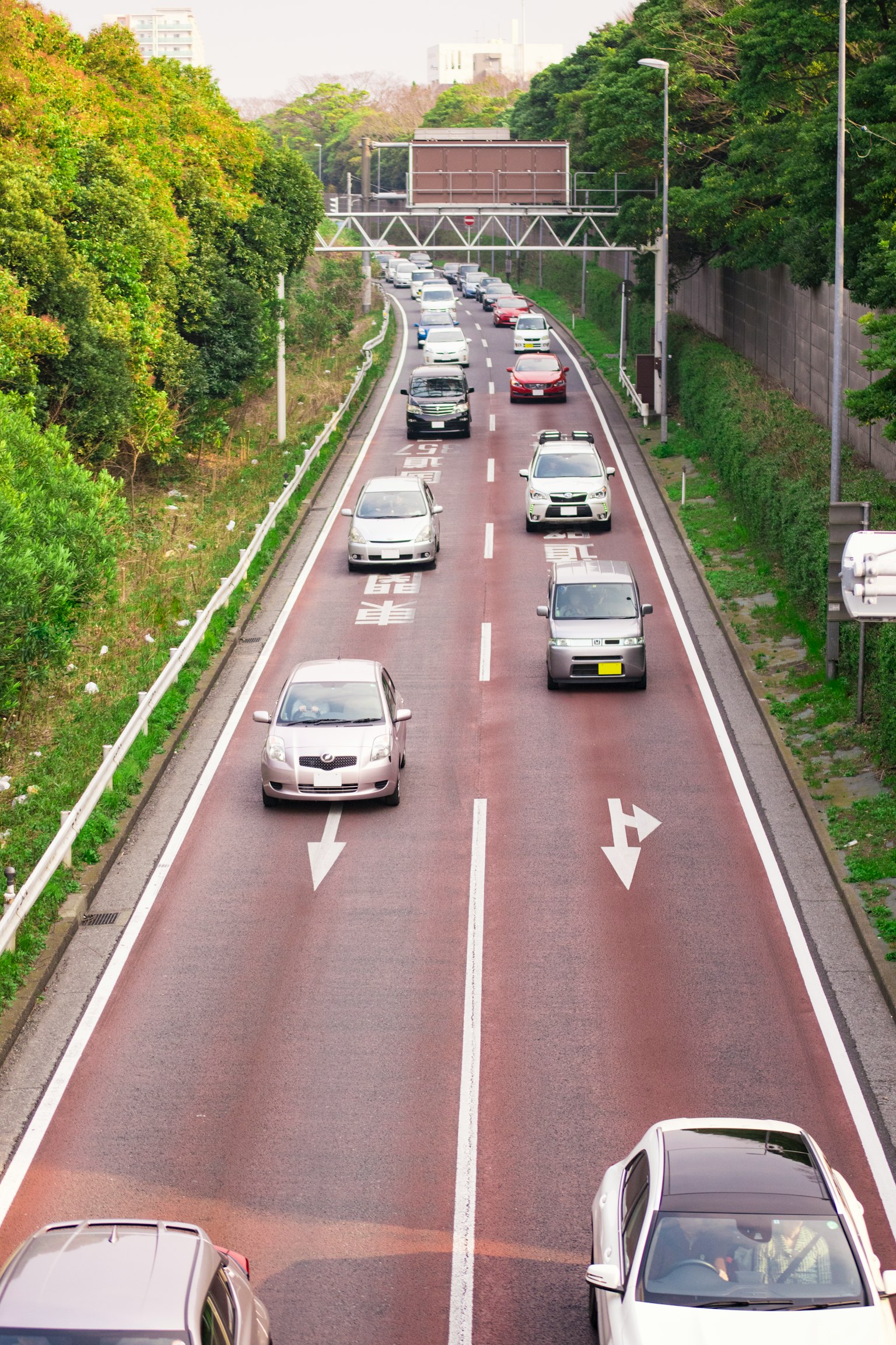 Vista di una strada urbana con auto in movimento circondata da alberi verdi e segnali stradali