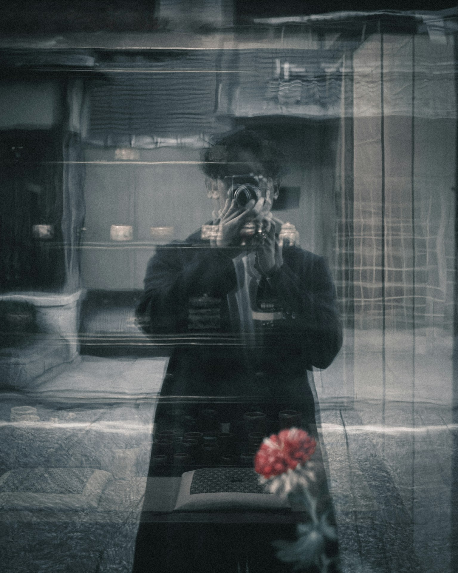 Foto hitam putih yang menunjukkan refleksi seseorang yang memegang kamera dengan latar belakang kabur