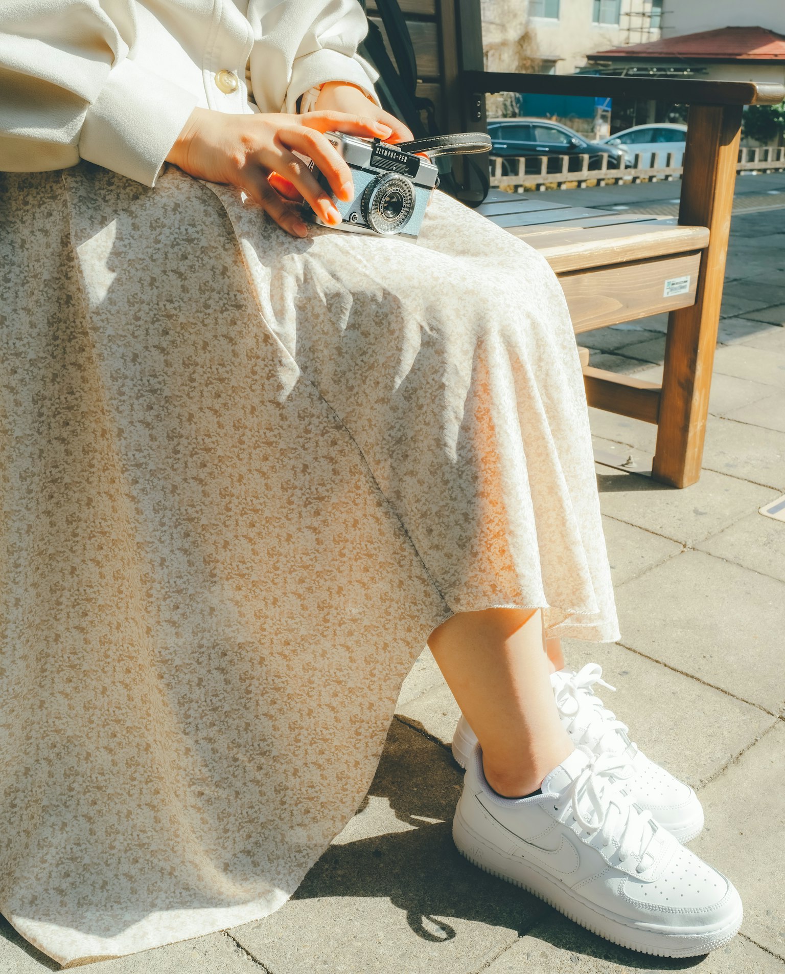 Pies de una mujer con zapatillas blancas y falda floral en un entorno al aire libre